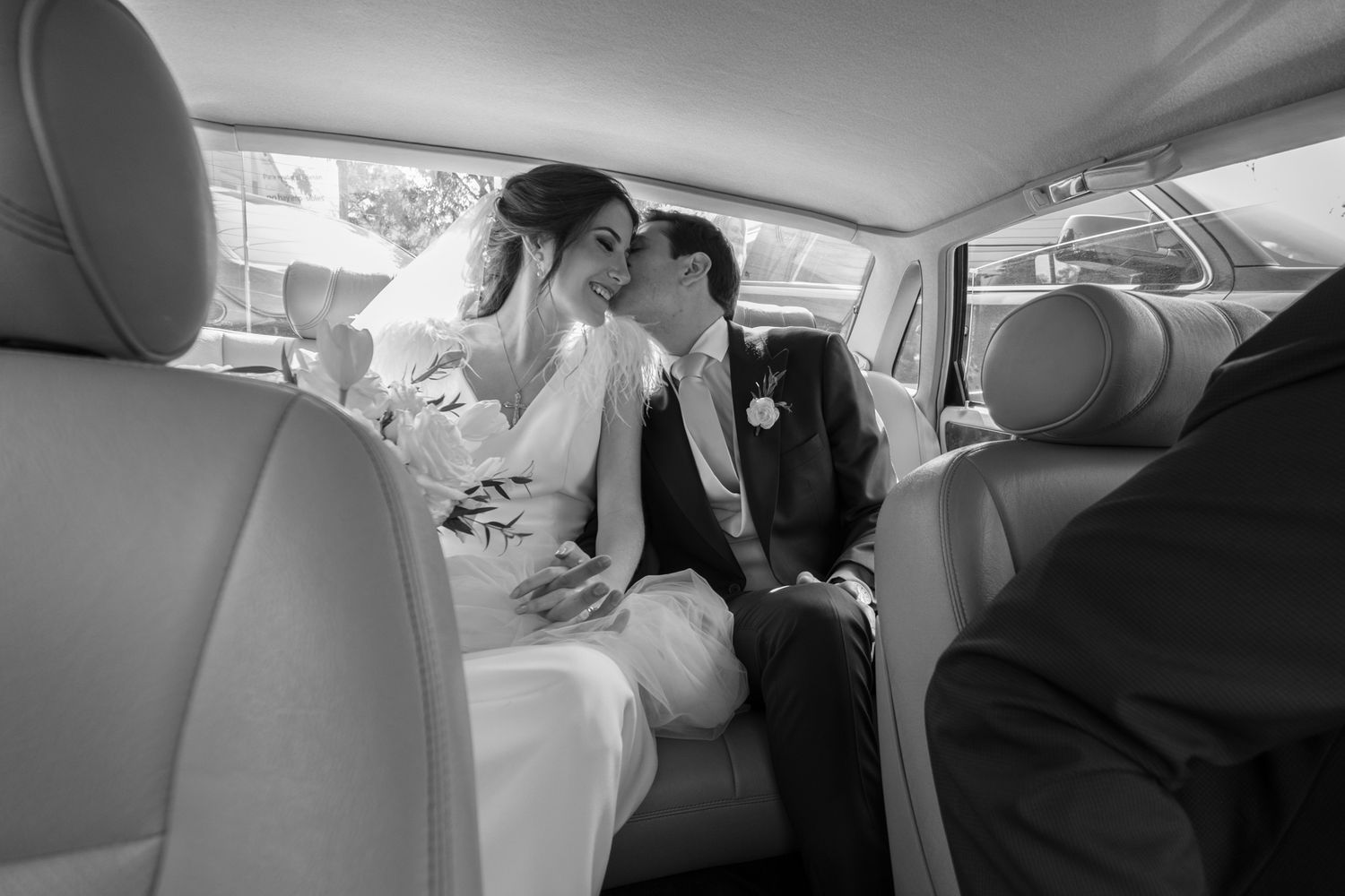 A black and white photo showing a couple in the back seat of a car after a wedding ceremony.