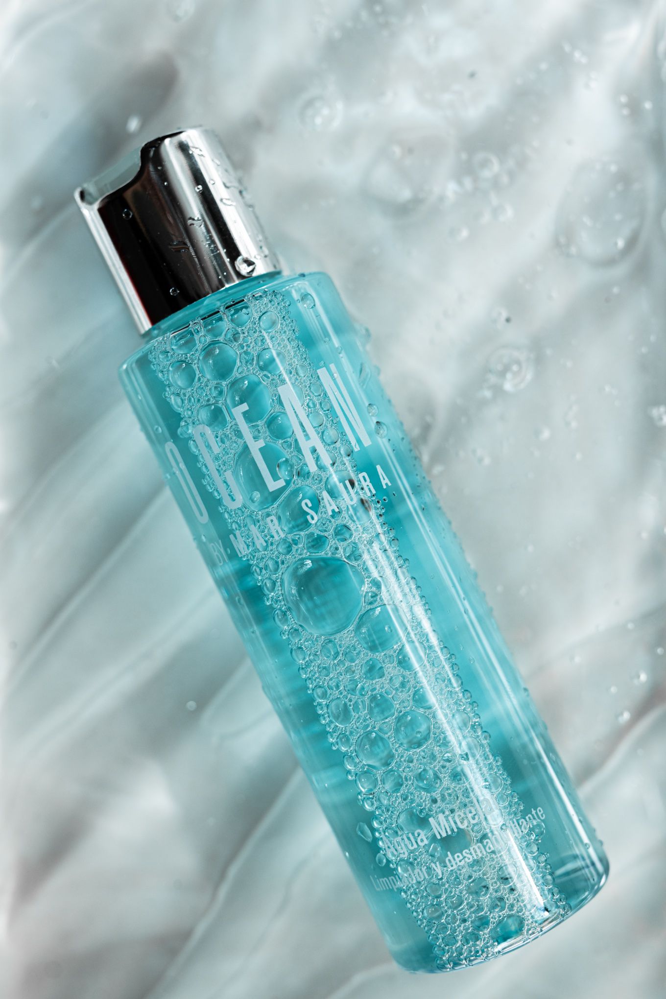 Turquoise beauty product bottle with bubbles and water droplets in macro photography.