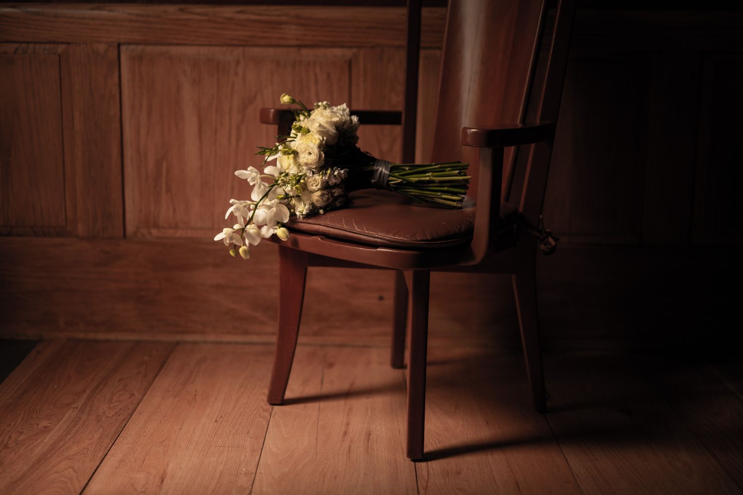 Elegant white floral arrangement on wooden chair in moody lighting.