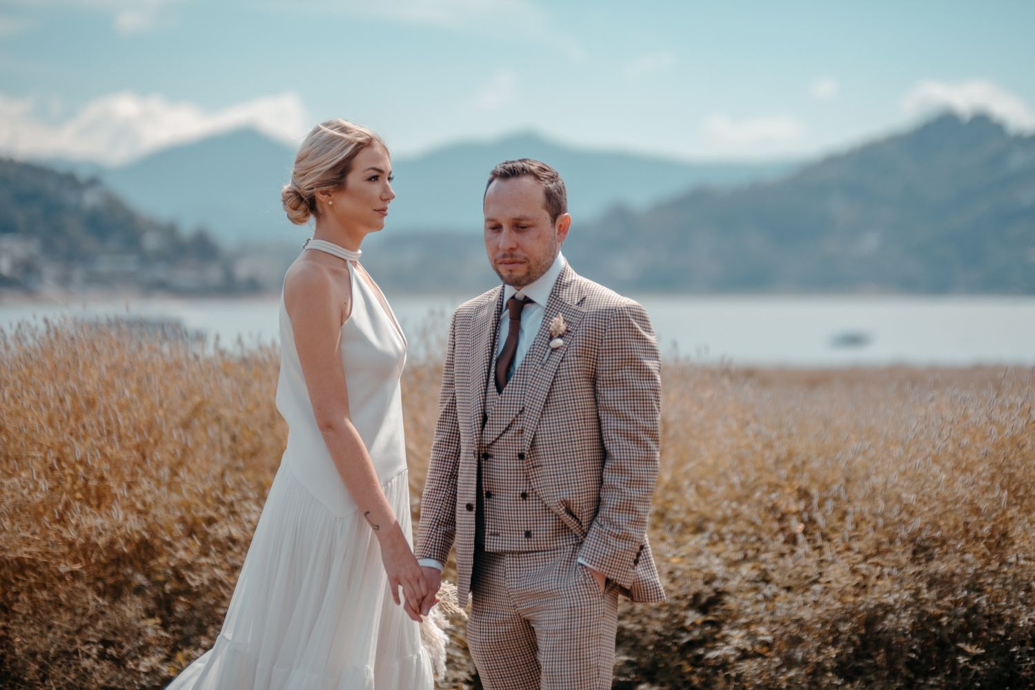 Elegant wedding couple posing in mountain meadow with lake view.