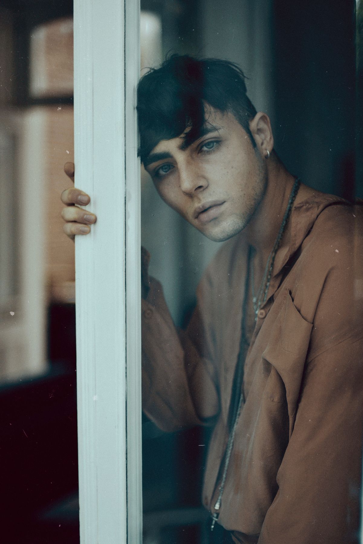 Atmospheric portrait through window frame with person wearing brown jacket.
