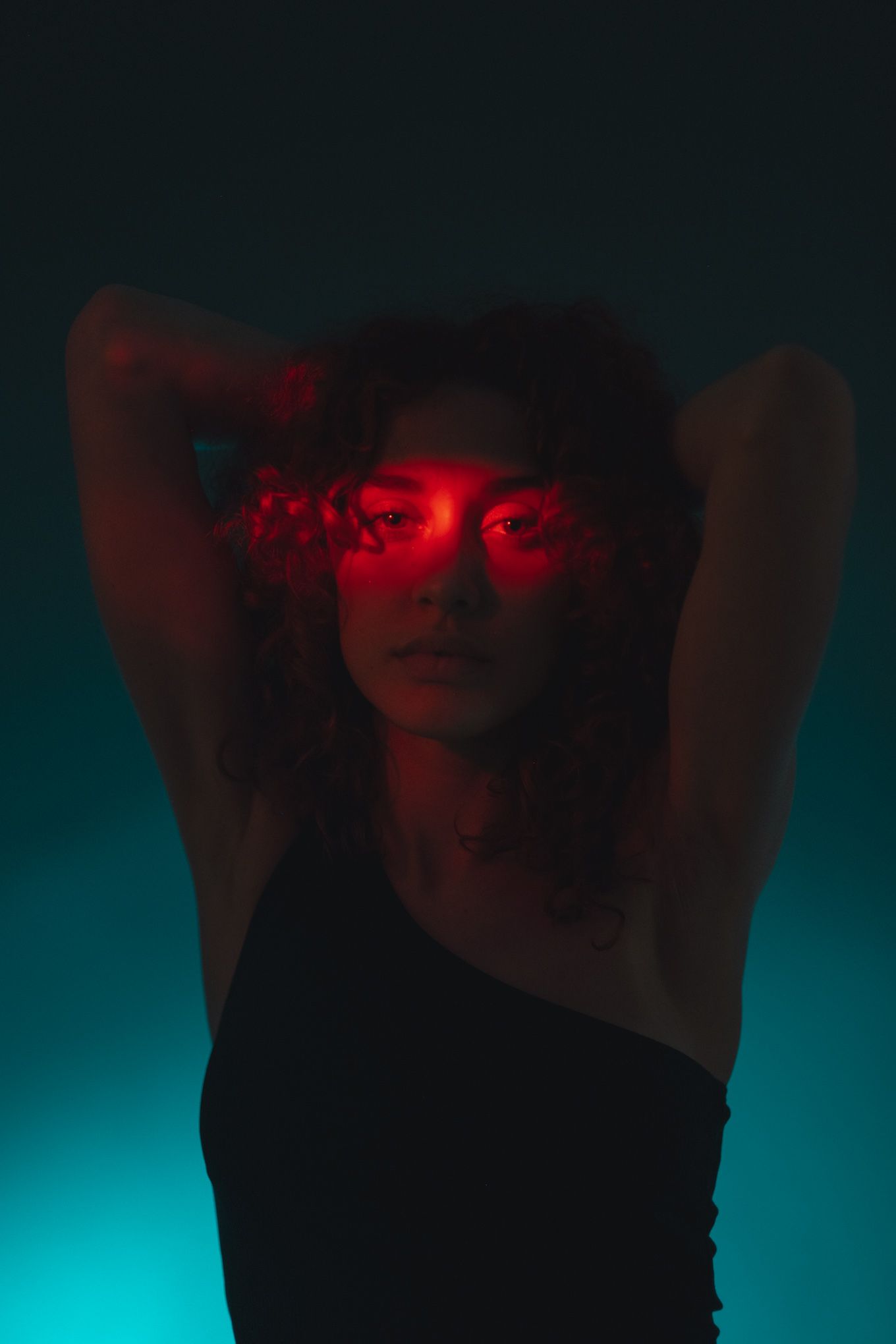 Dramatic portrait with red lighting and teal background creating otherworldly atmosphere.