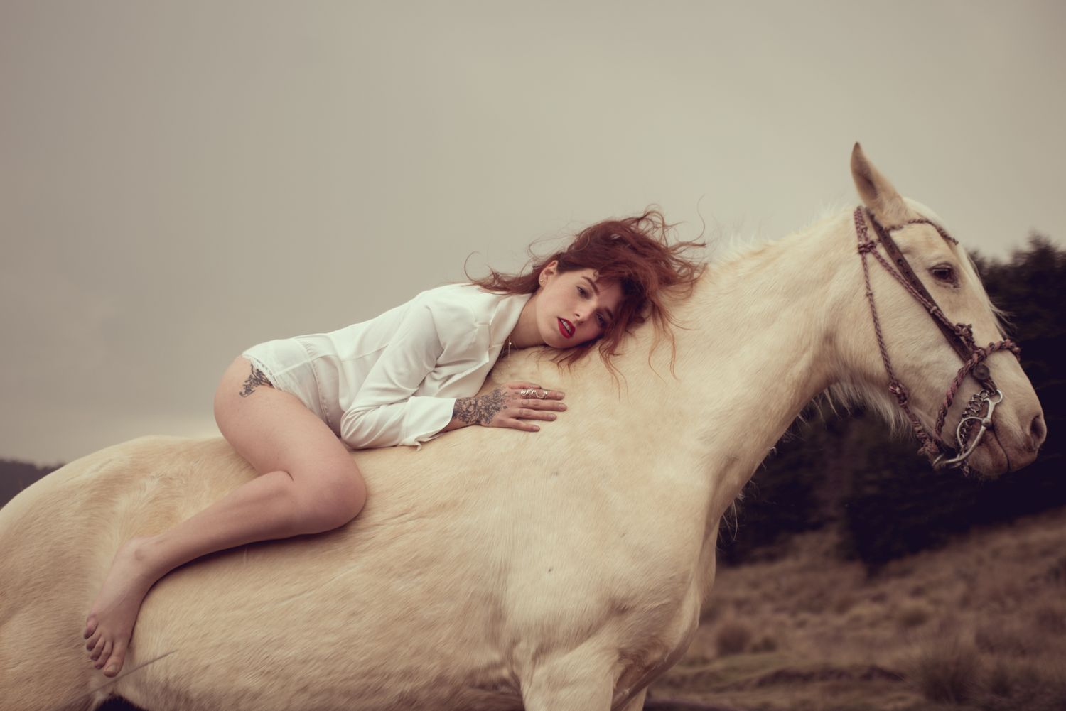 Dreamy portrait of woman lying on white horse's back in natural setting.