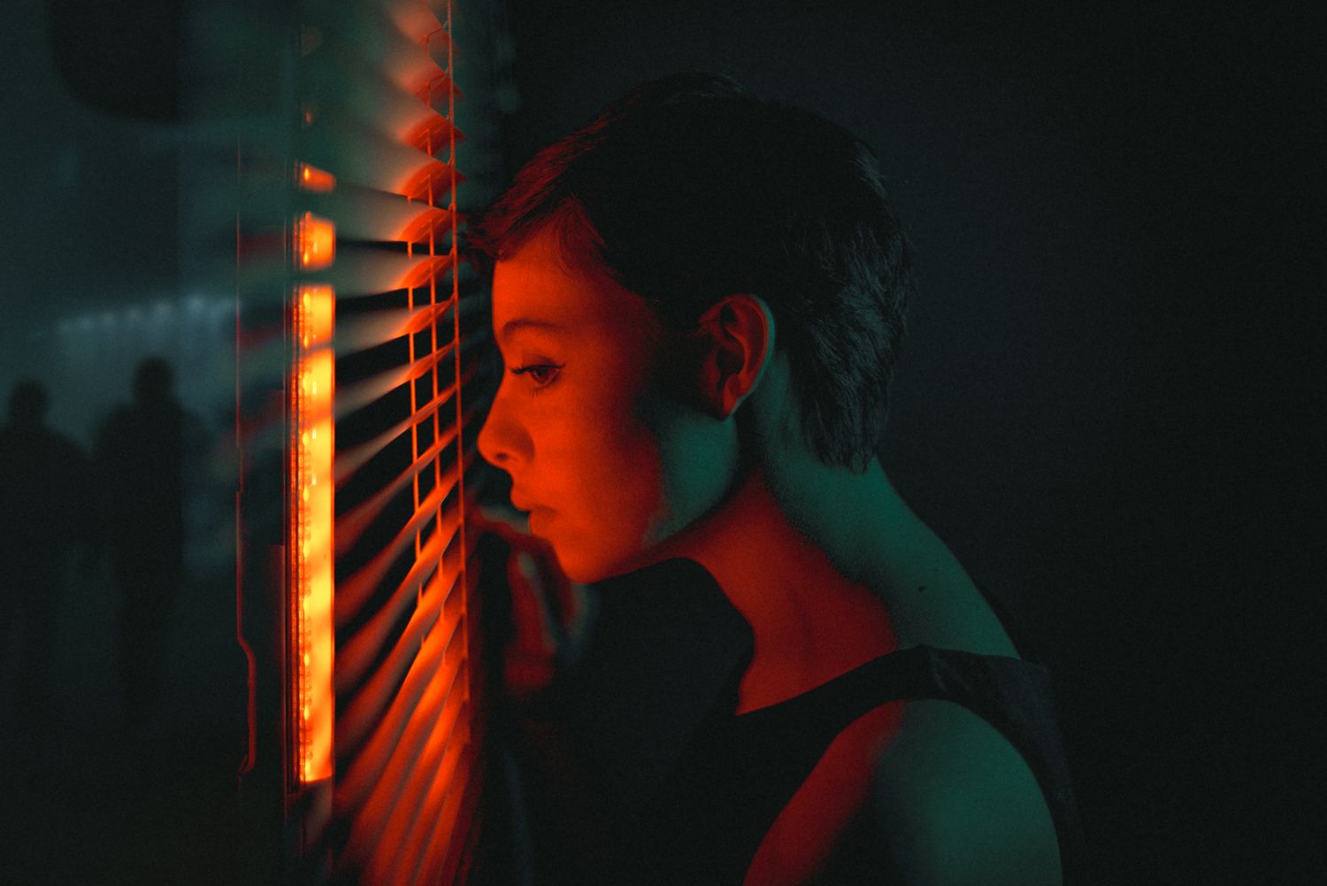 Atmospheric side profile portrait with orange and teal lighting through window blinds.