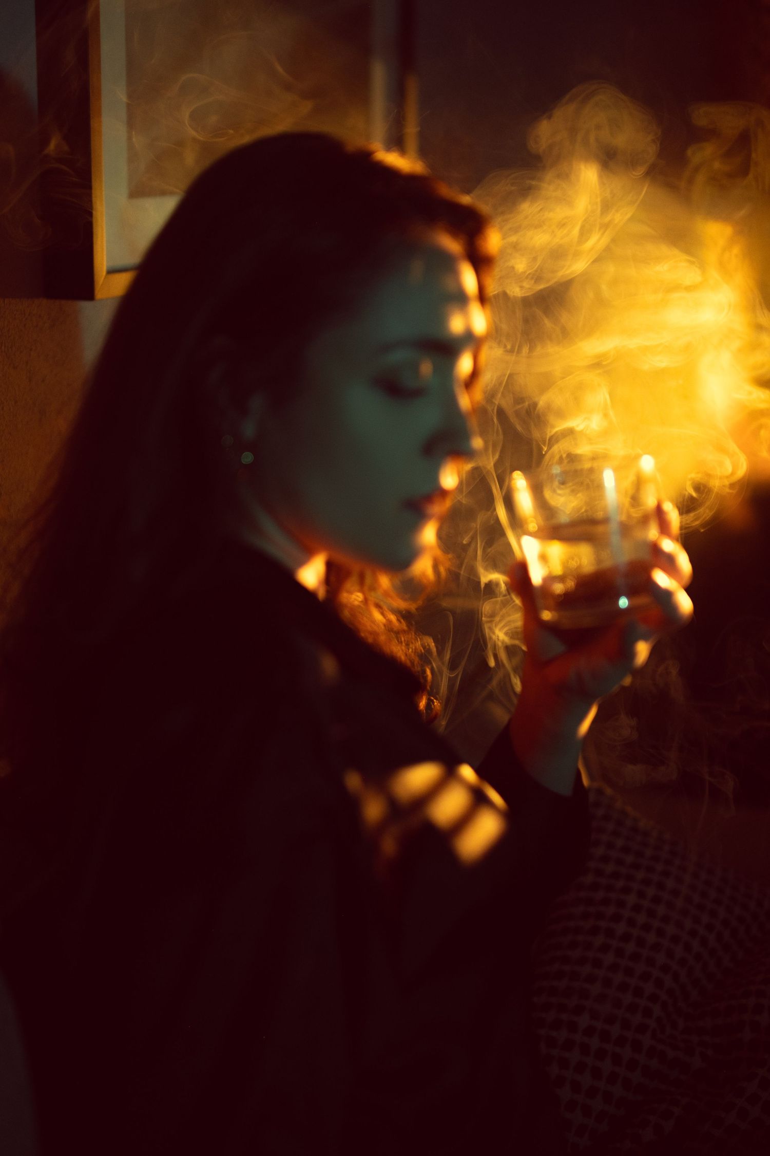 Atmospheric portrait in warm lighting showing a silhouette exhaling smoke in a dark moody setting.