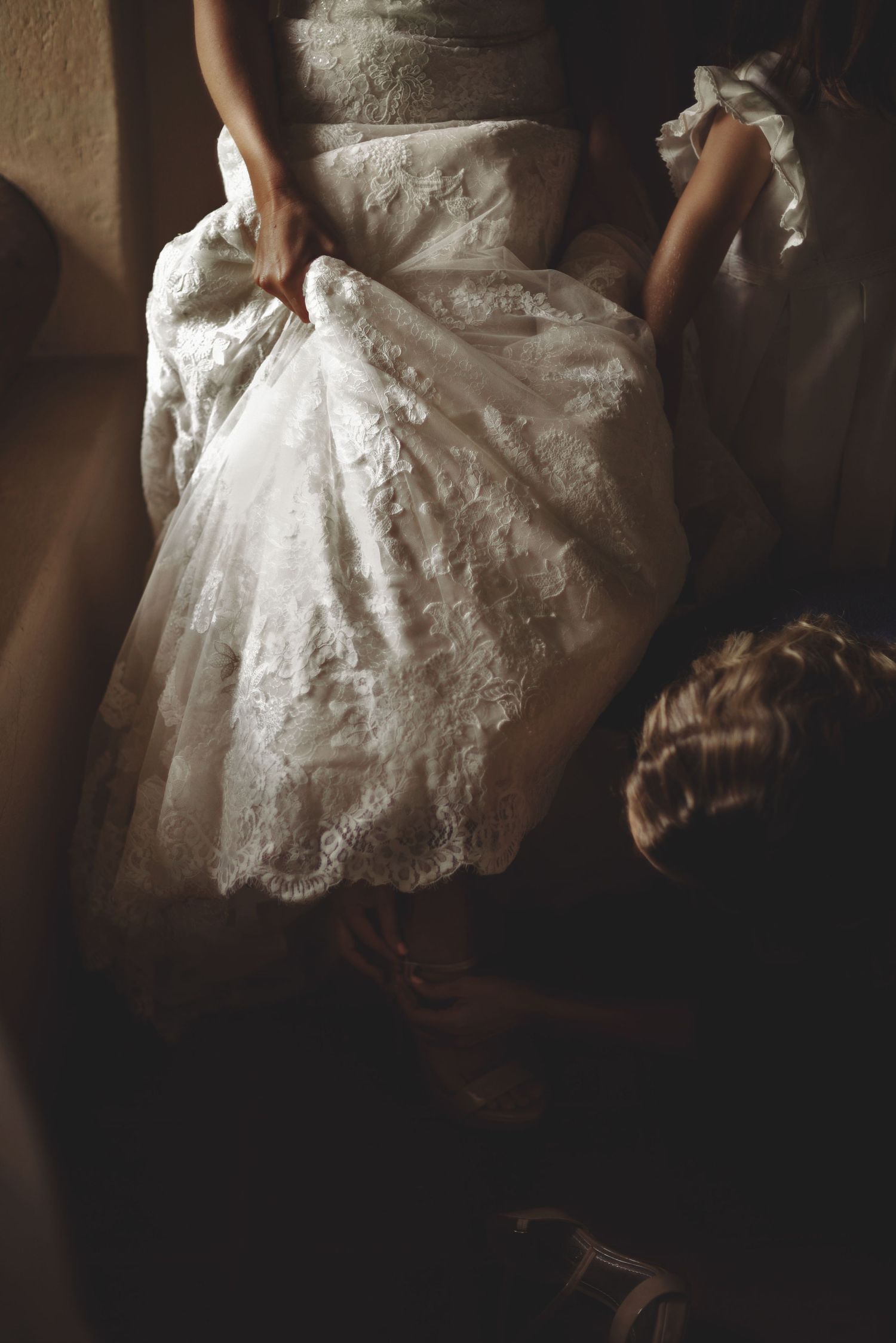 A white lace wedding dress with intricate details captured in a moody, atmospheric lighting setting.