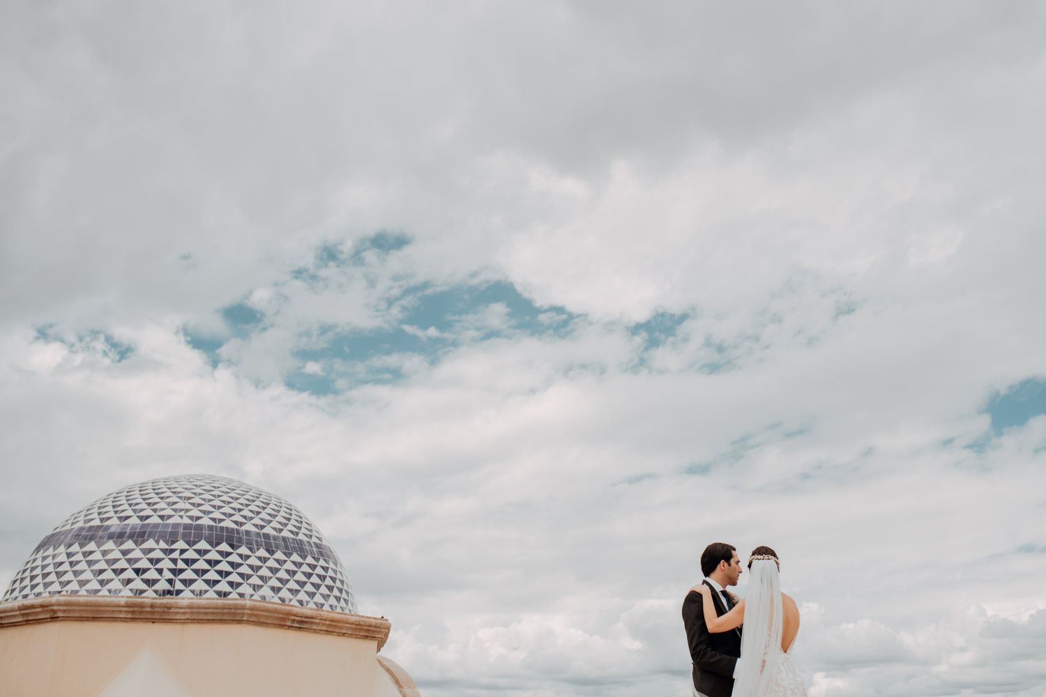 Minimalist architectural photo showing a domed structure against cloudy sky with two figures in the distance.