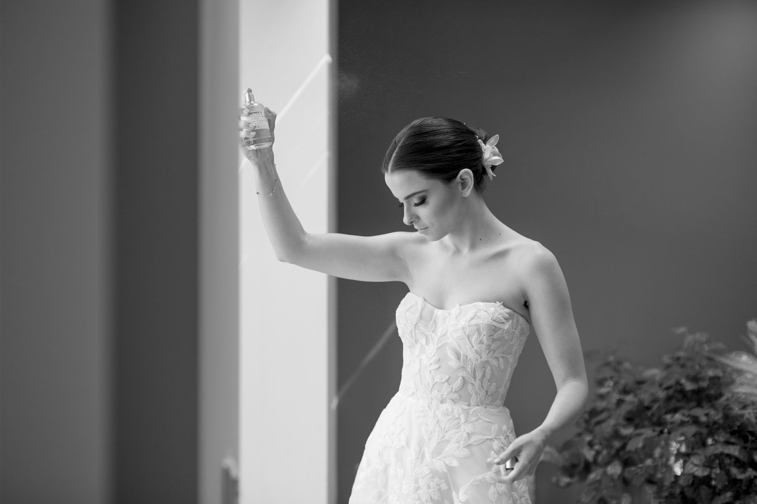 A bride in a strapless lace wedding gown stands elegantly against a wall in a black and white portrait.