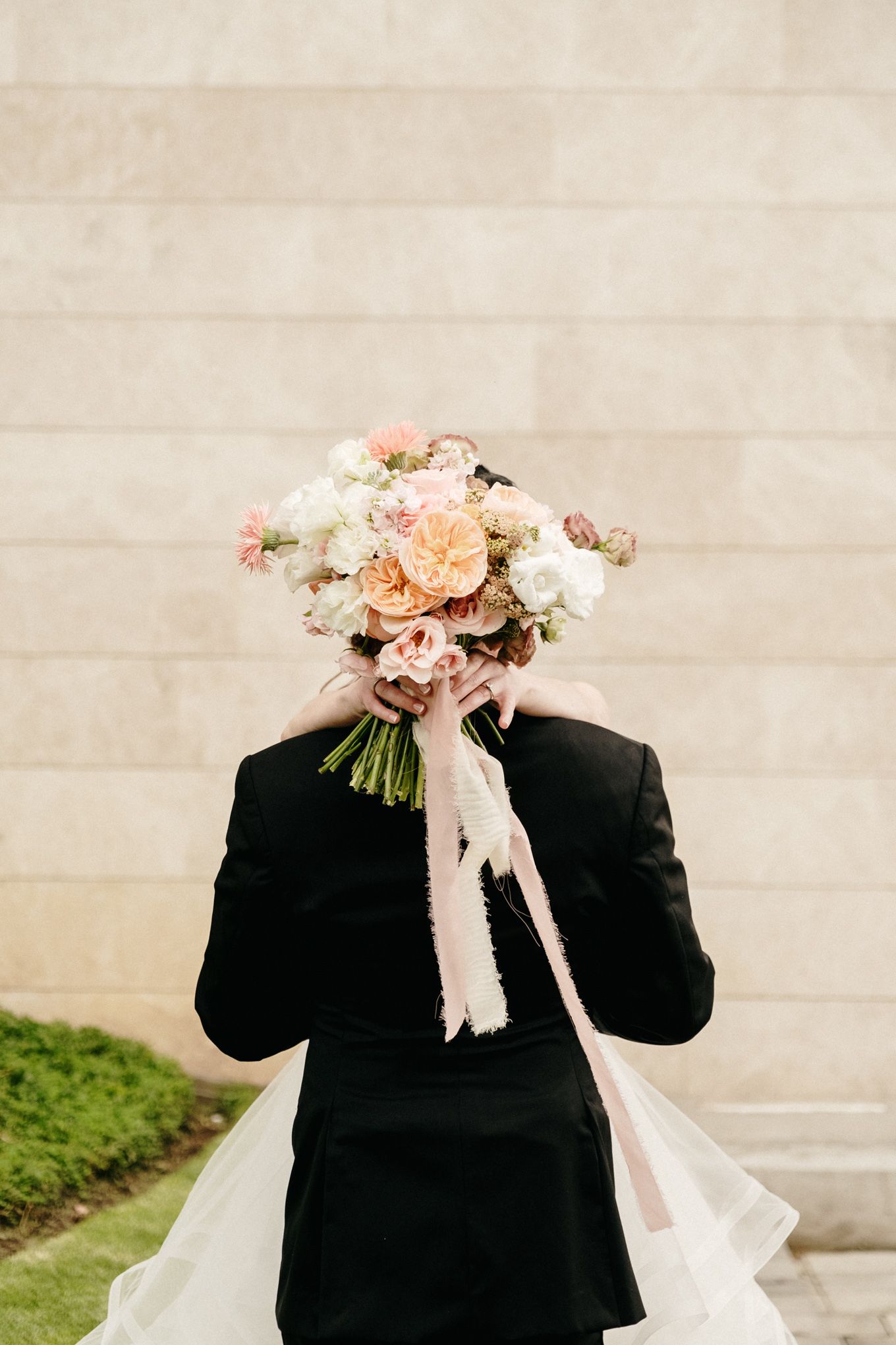 Wedding couple playfully poses with bouquet of blush roses covering their faces.