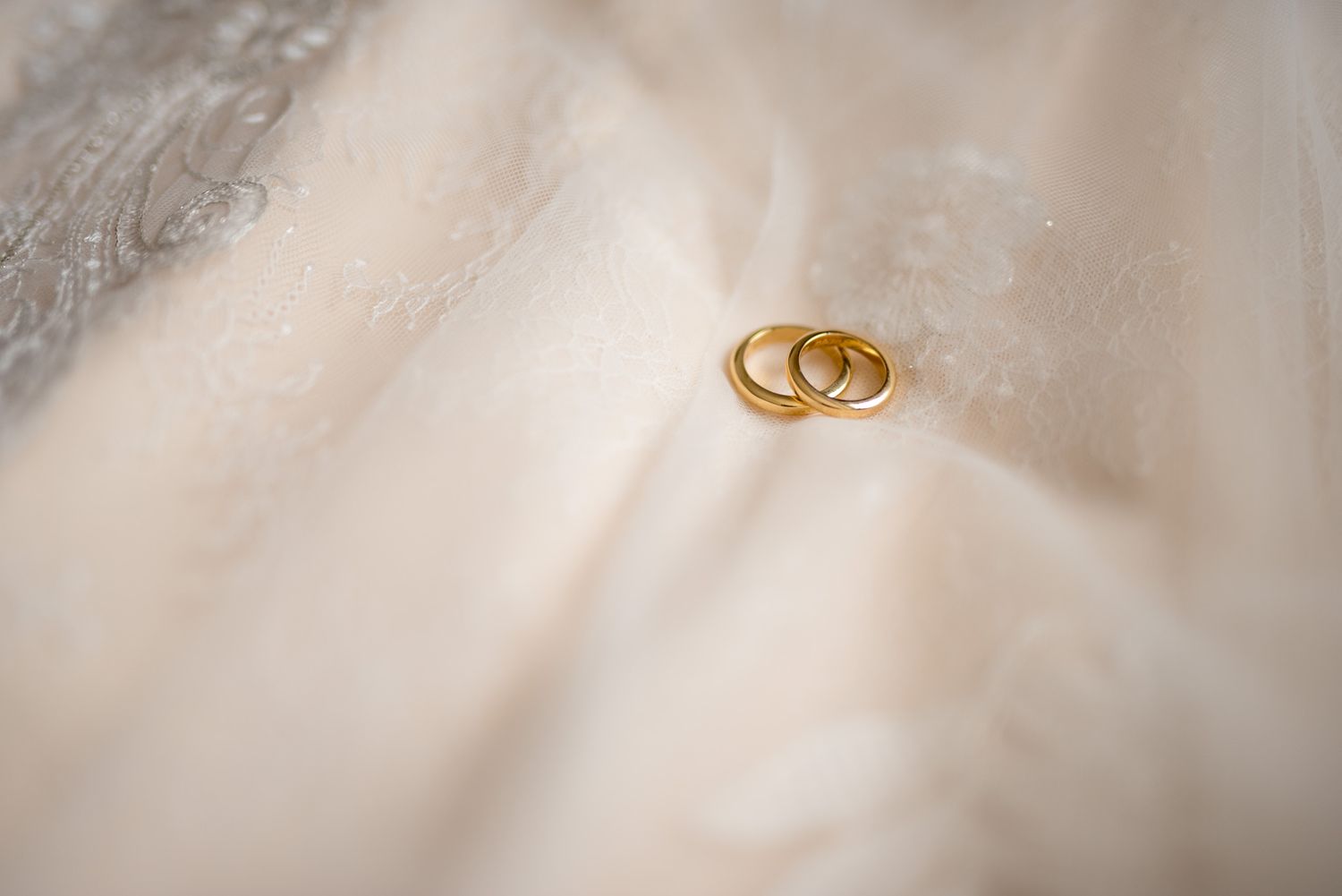 Two golden wedding rings photographed on white fabric with soft lighting.