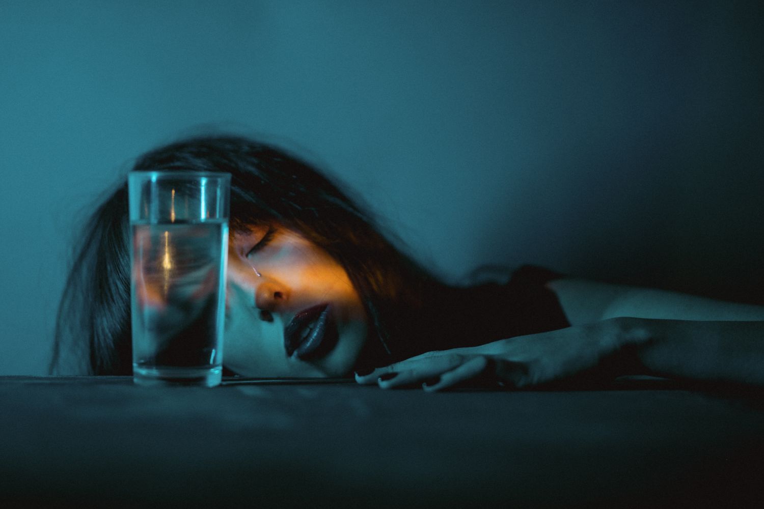 Side view portrait with glass of water under atmospheric teal lighting.