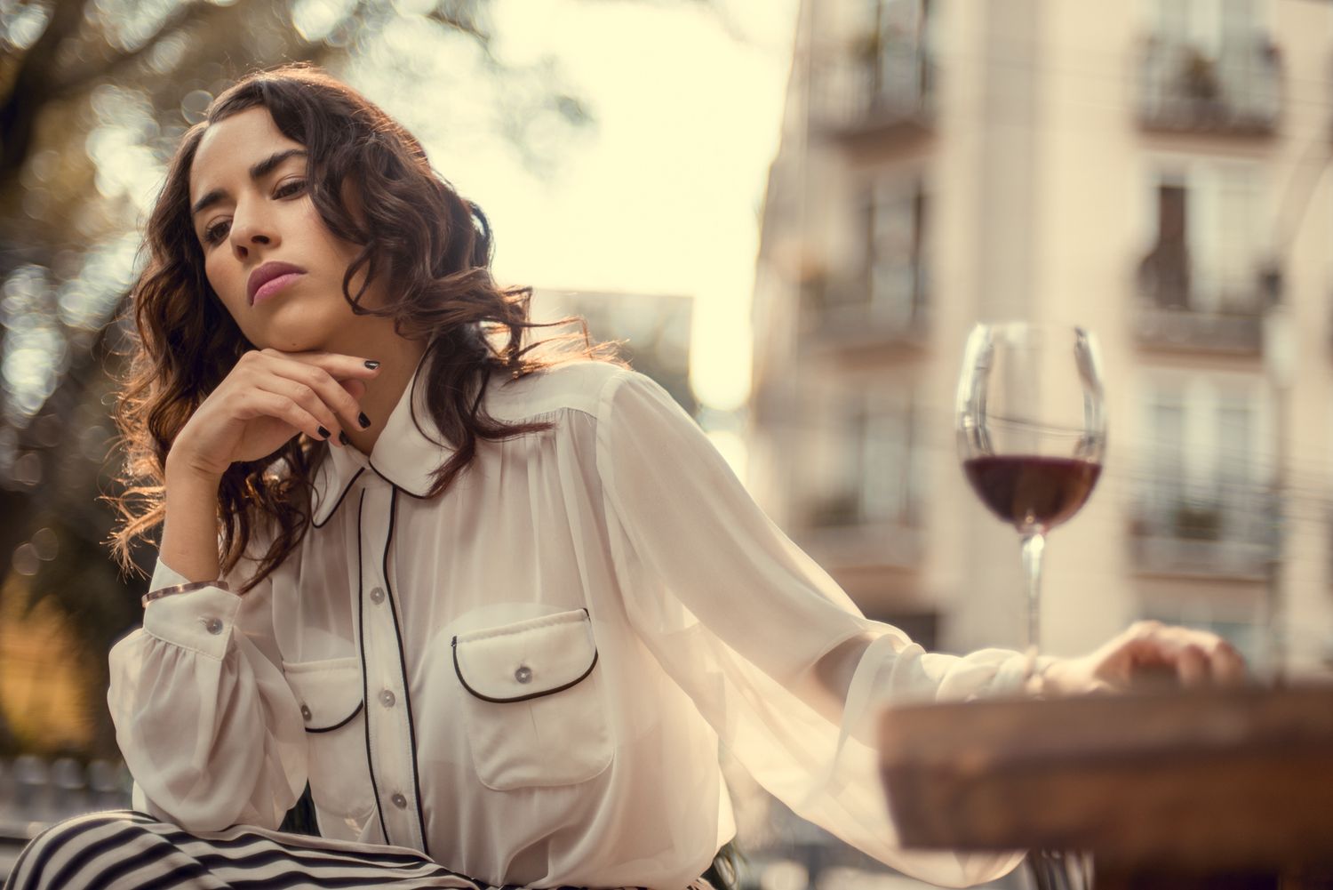 Elegant lifestyle shot with white blouse and glass of red wine on balcony at sunset.