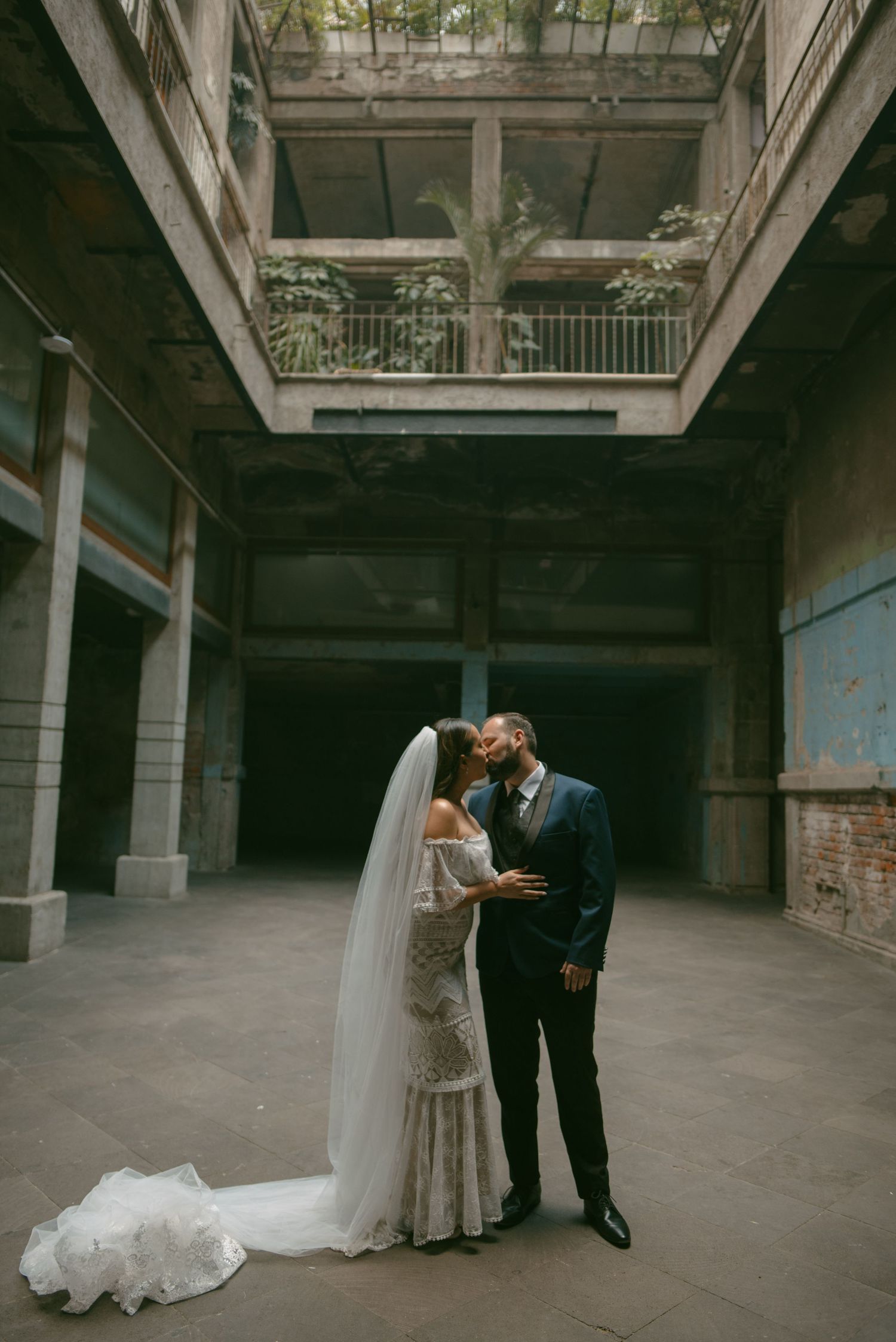Wedding couple embracing in an industrial venue with long flowing veil and exposed brick walls.