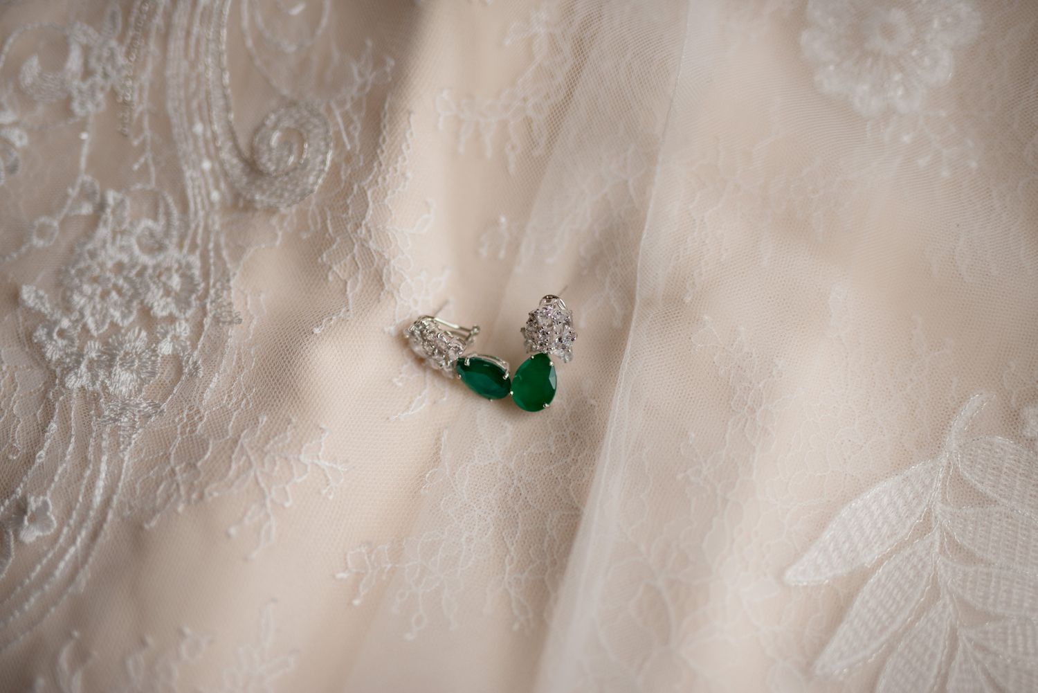 Emerald and diamond earrings photographed on delicate white lace fabric.
