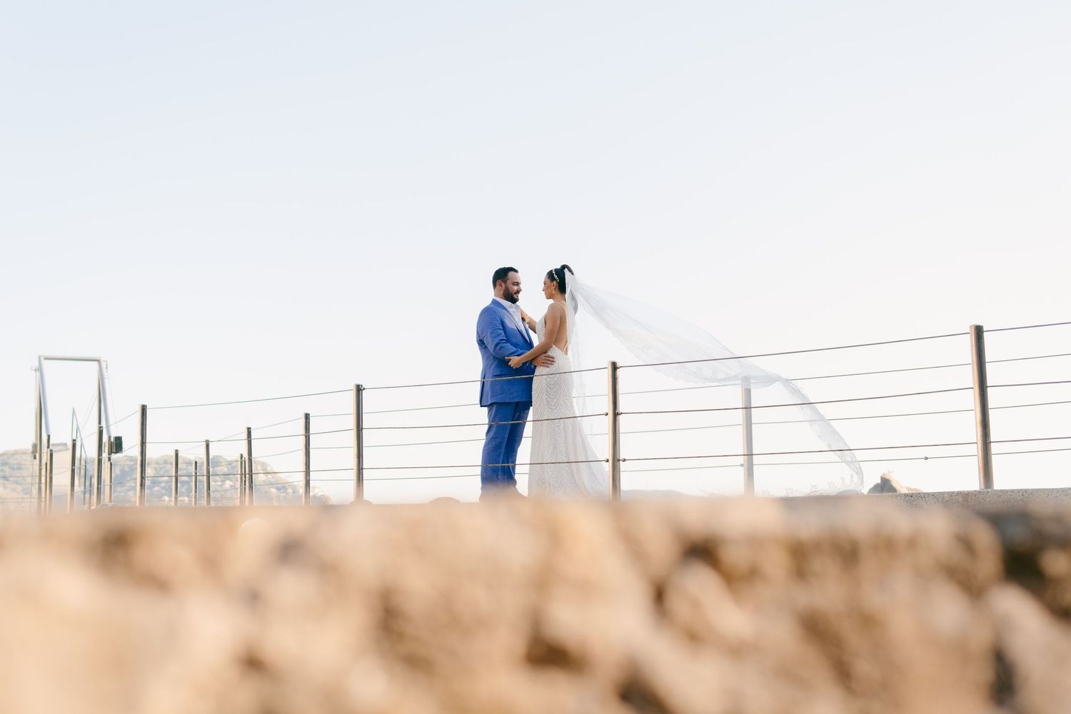 Wedding couple stands together on elevated boardwalk against bright sky.