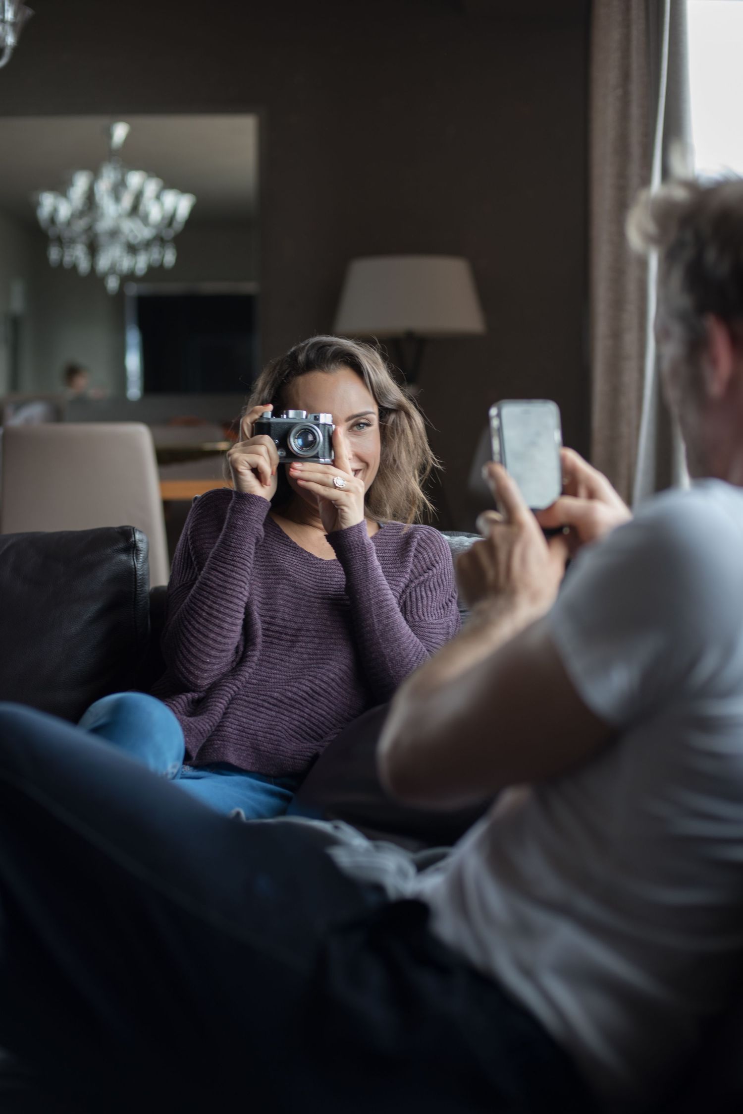 A candid moment of someone taking a photo while another person uses their phone on a couch.