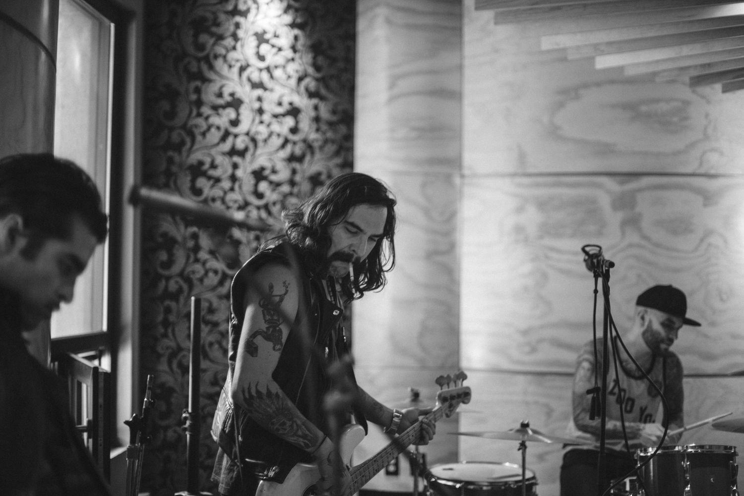 Wide shot of band members performing in studio with dramatic lighting and wallpaper background.