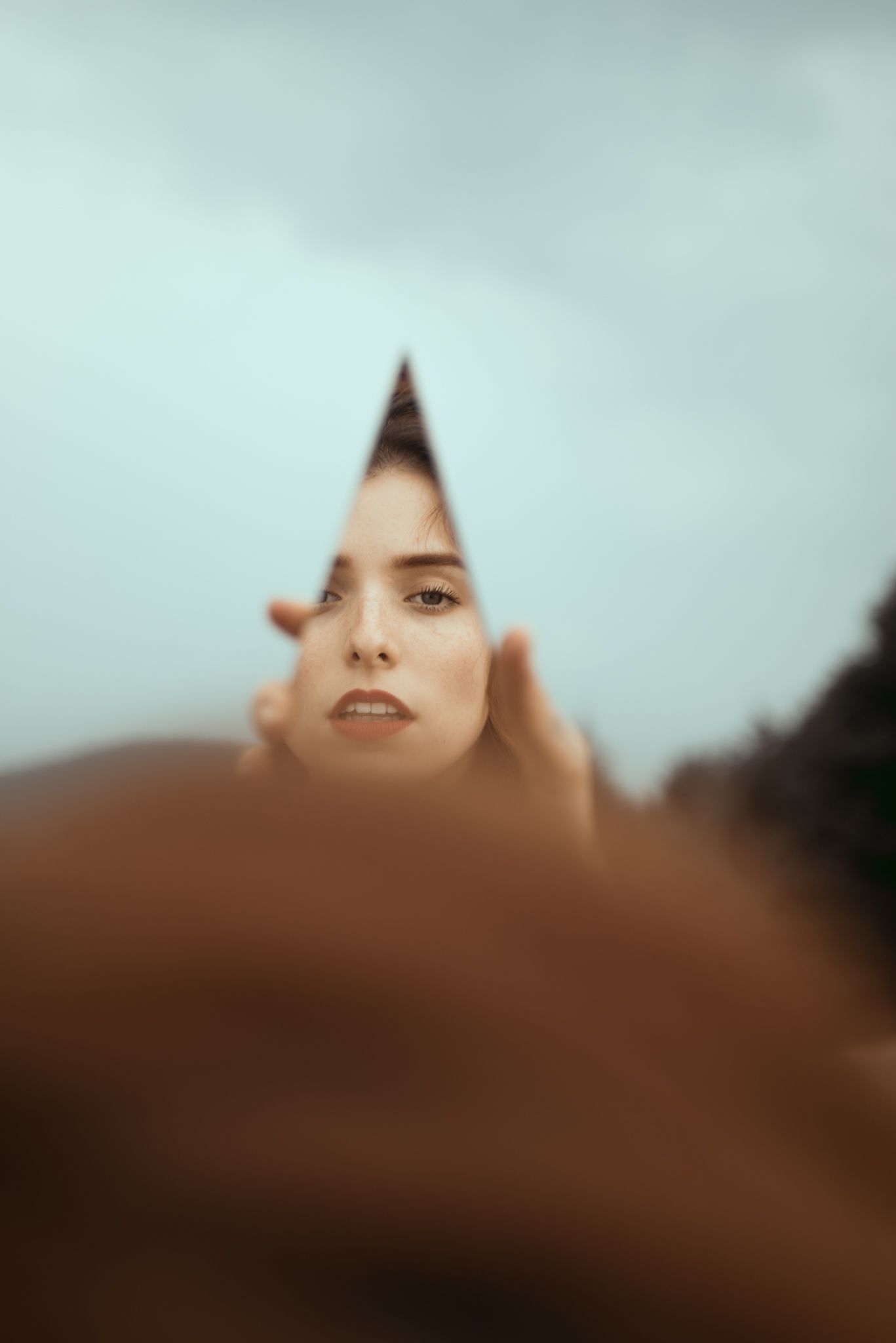 Abstract triangular reflection portrait against a muted sky backdrop.