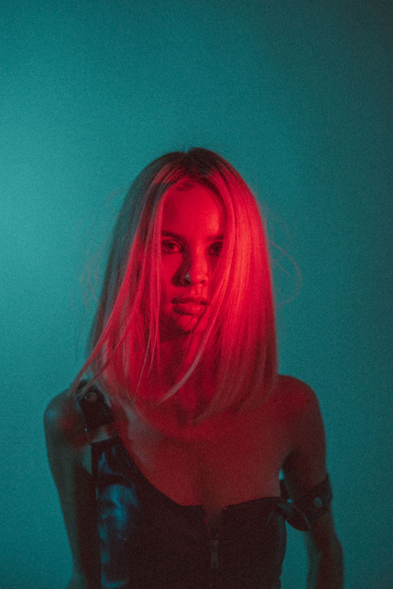 Portrait bathed in red light against teal background creating striking contrast.