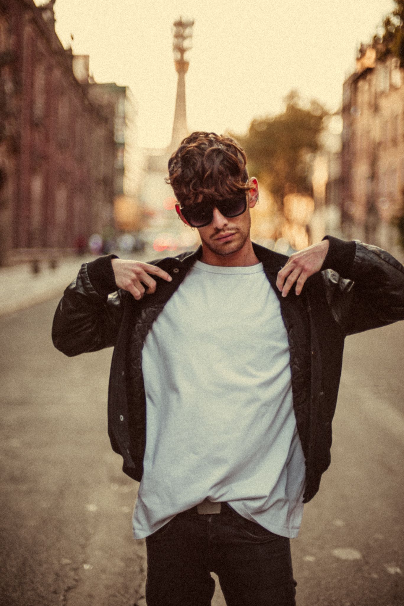 Urban fashion portrait of person in leather jacket and sunglasses on city street at golden hour.