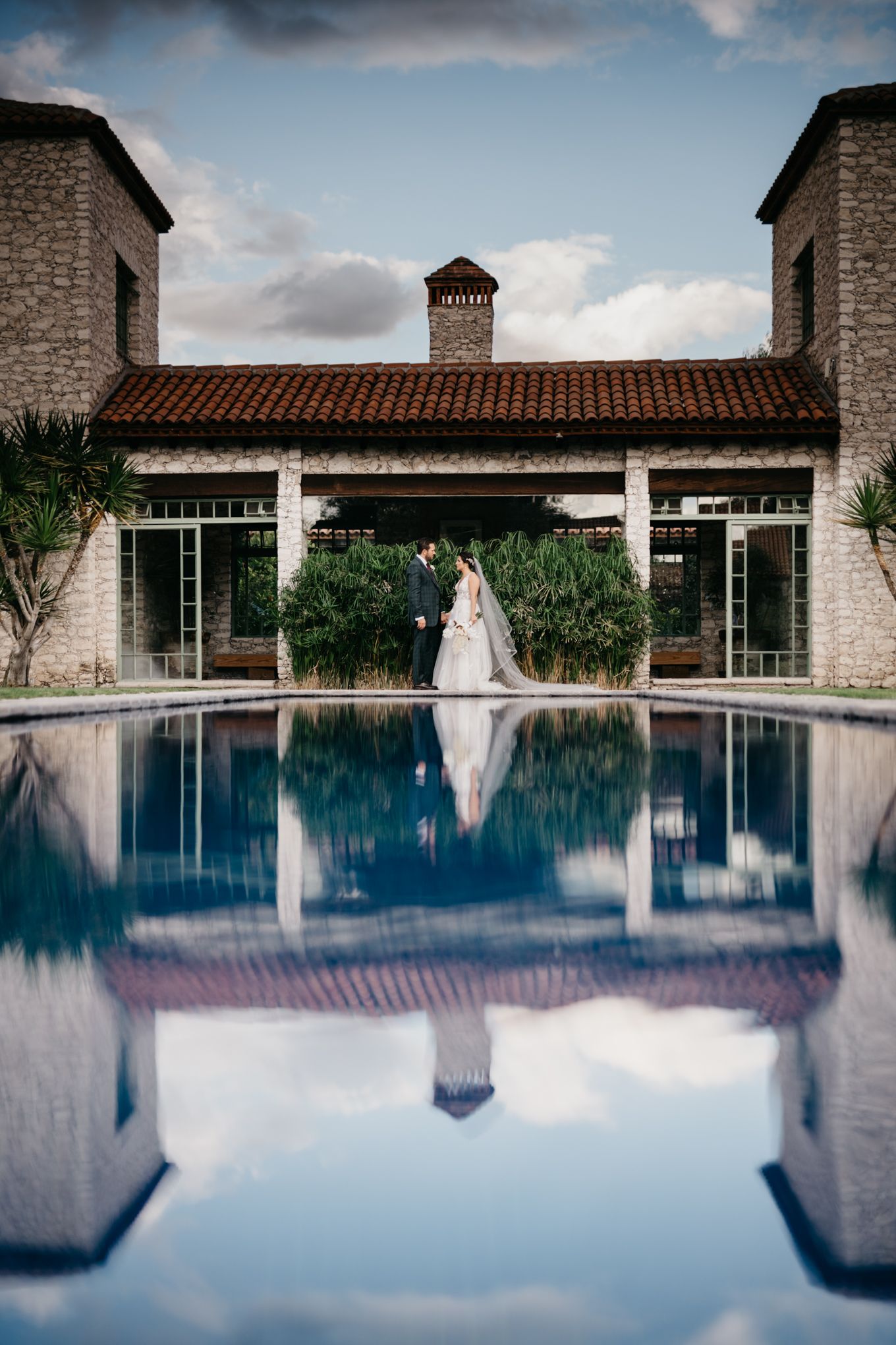 Elegant stone building with swimming pool reflecting architecture and sky in luxurious resort setting.
