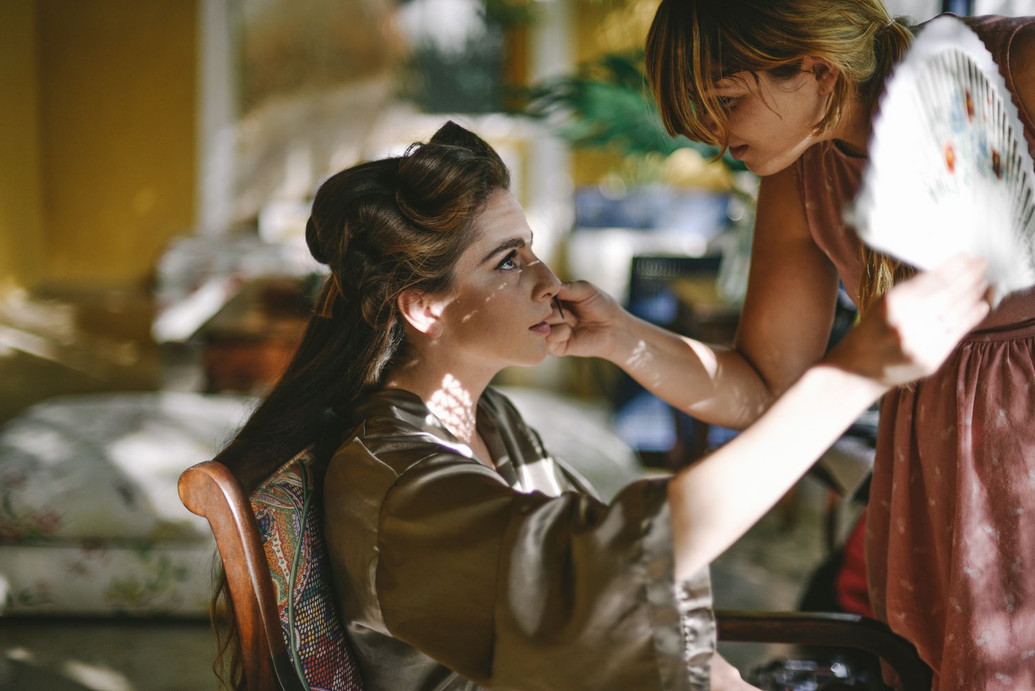 A makeup artist applies cosmetics to a person sitting in a vintage-style chair during preparation for an event.