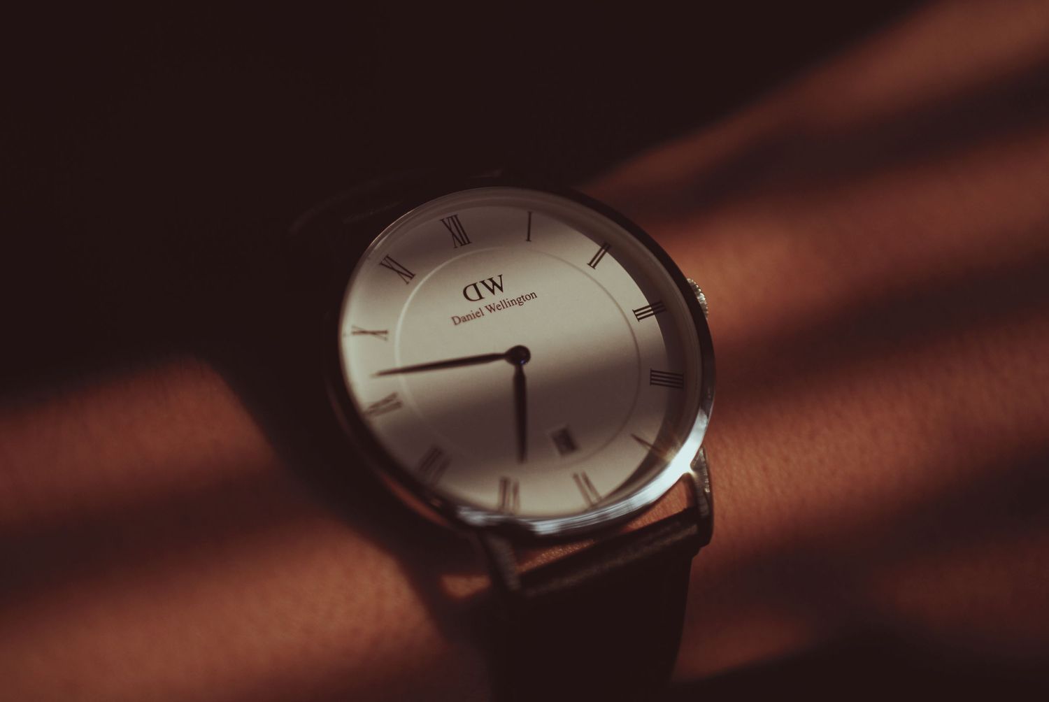 A stylish analog wristwatch with round face and brown leather strap photographed in dramatic lighting.