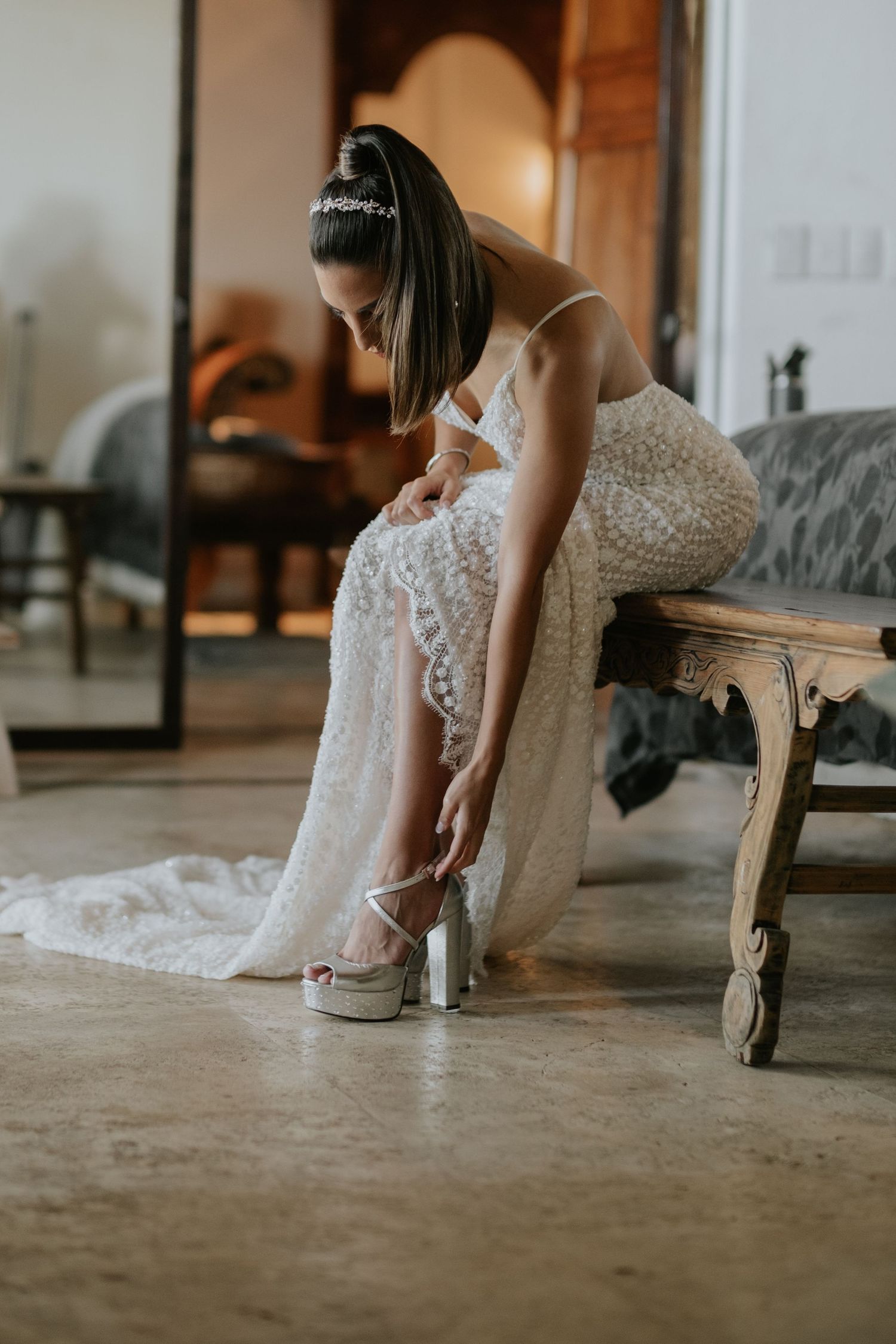 Bride adjusting wedding shoes while sitting on antique chair.