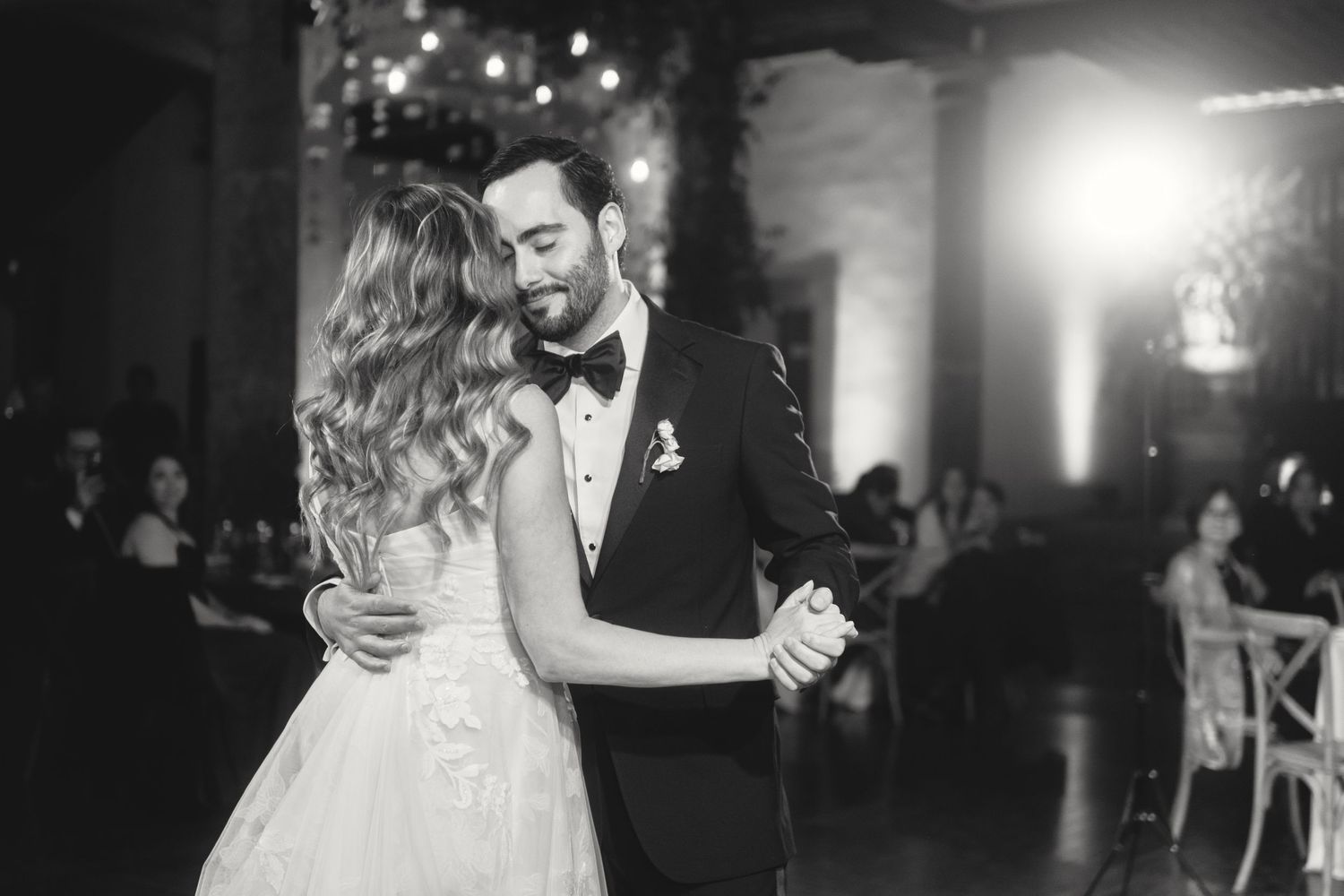 Romantic first dance moment captured in black and white with ambient lighting.