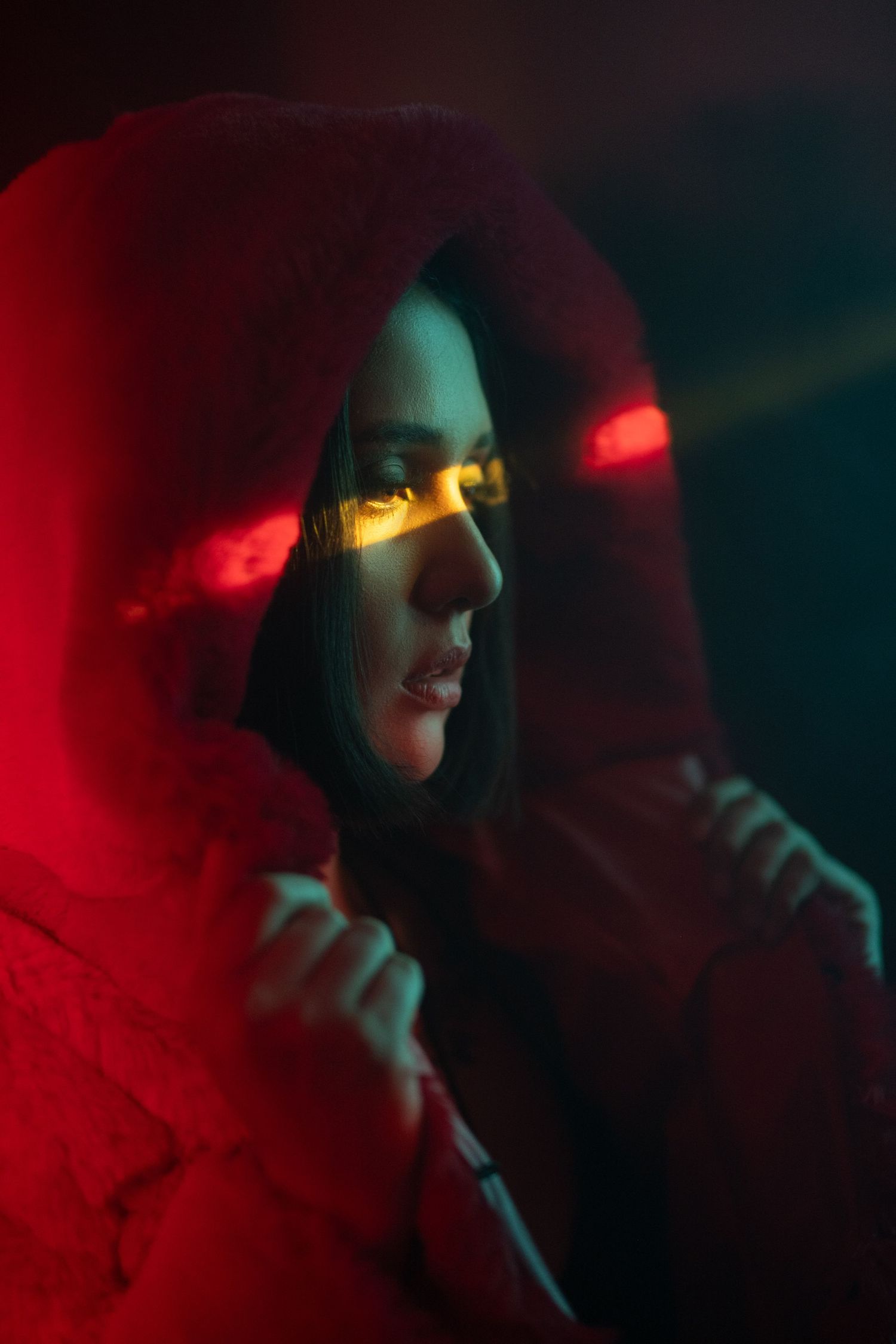 Dramatic side profile portrait in red hoodie under moody lighting with teal and crimson color accents.