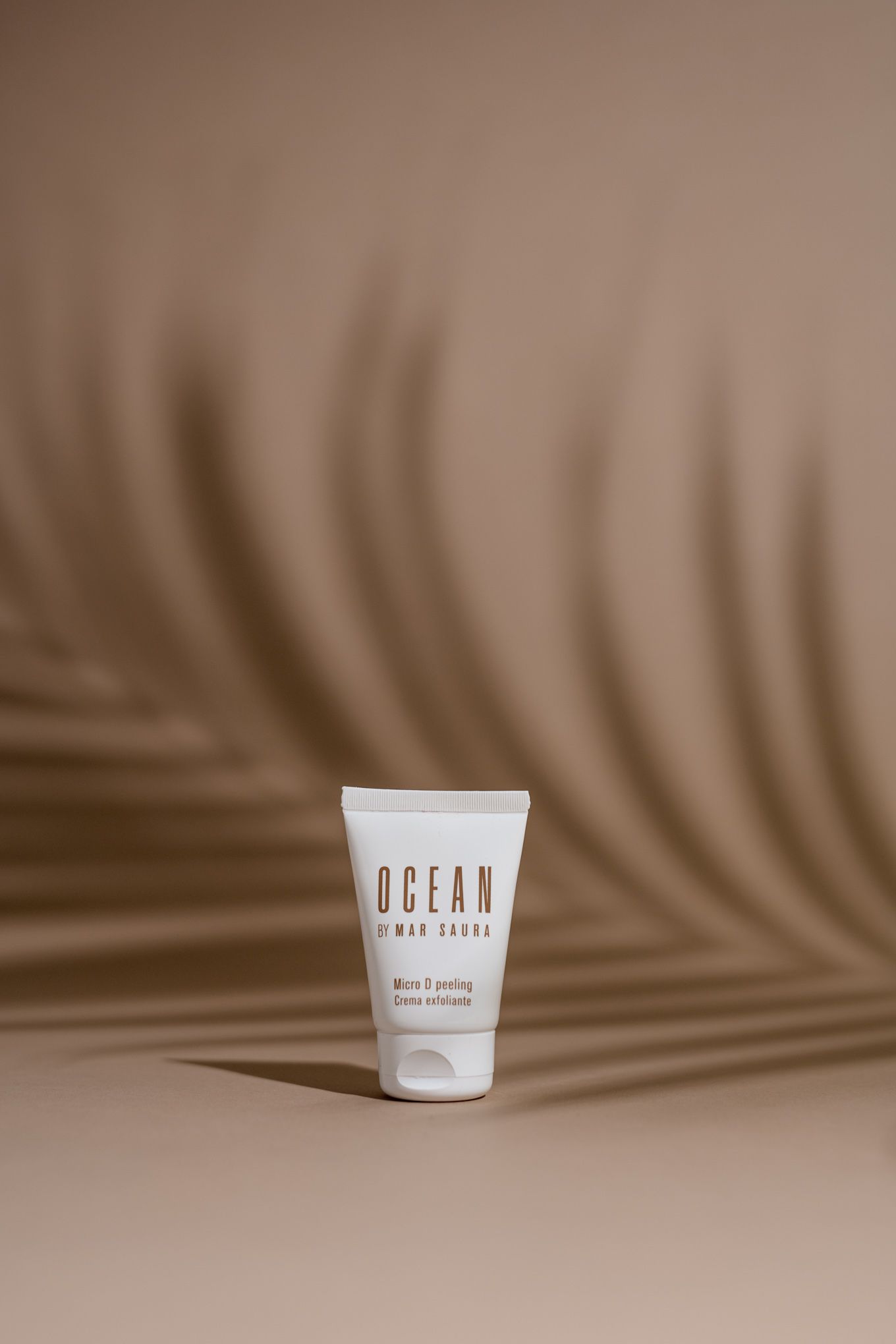 Minimalist cream tube product against beige background with palm leaf shadow.