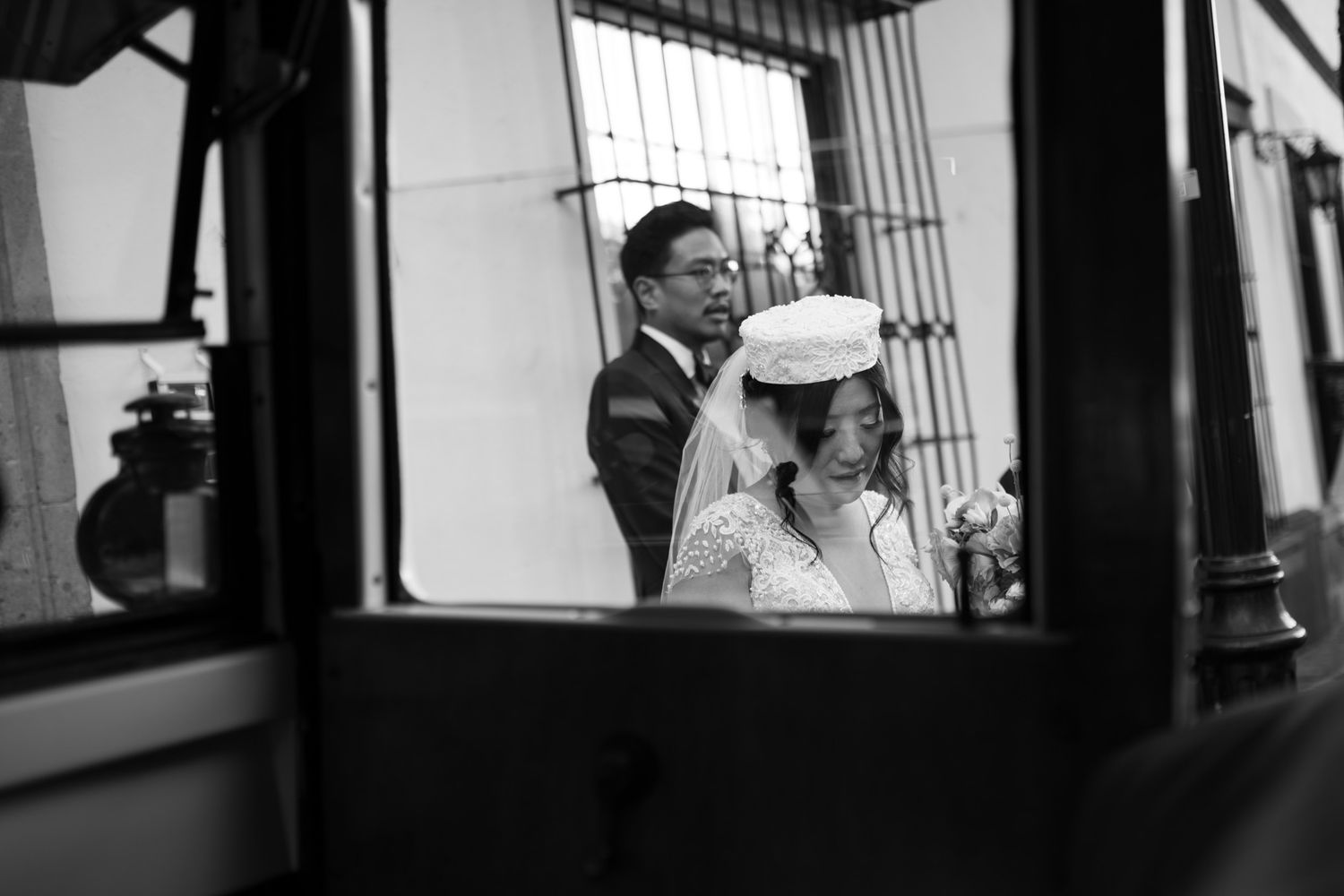 Black and white photograph showing passengers inside a train car window, viewed through a window frame.