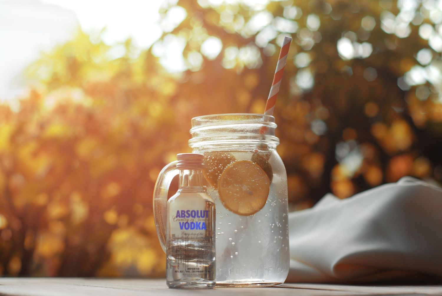 A mason jar filled with a creamy beverage and orange slice sits beside a small bottle in warm sunset lighting.