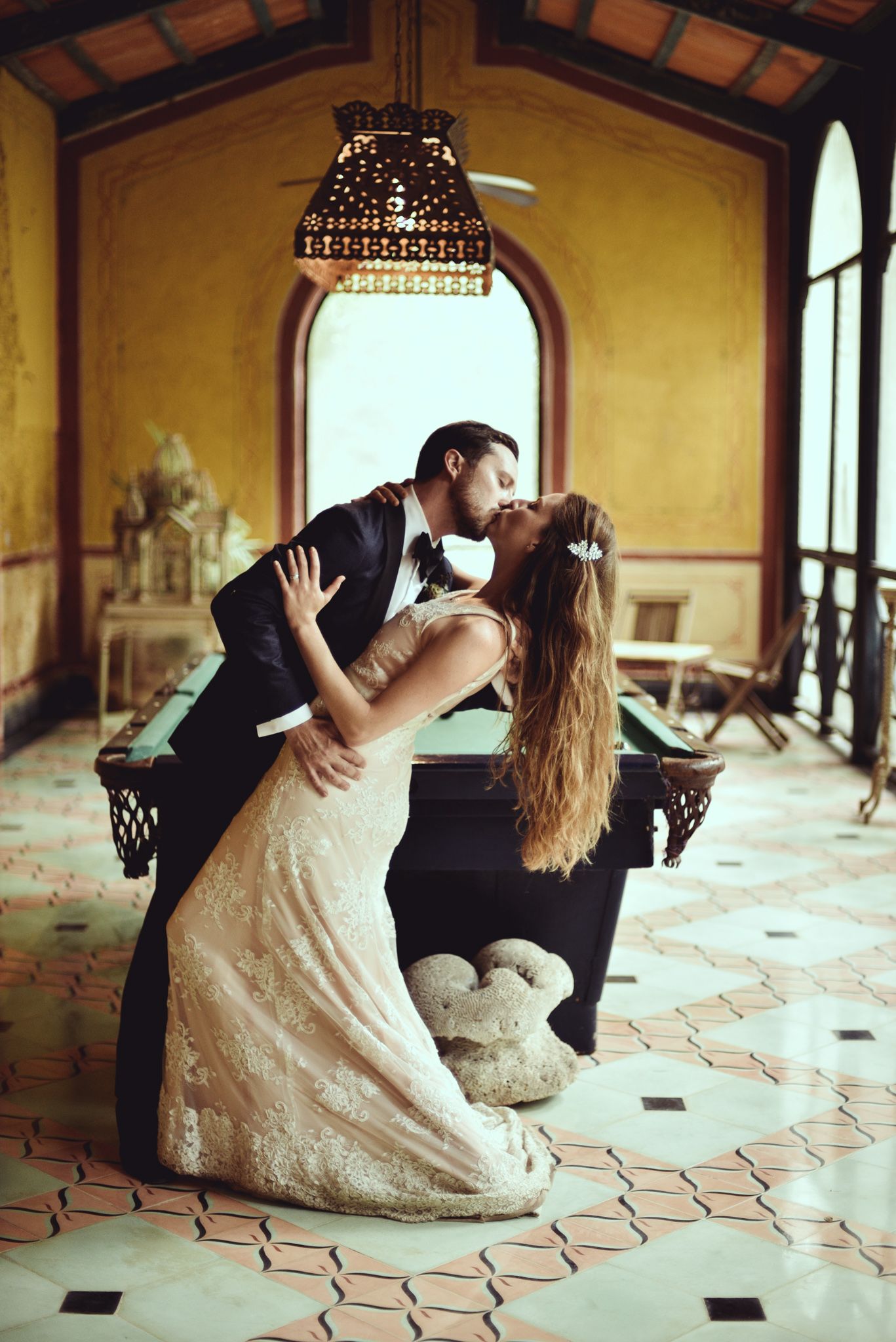 A romantic scene captured in a vintage villa with tiled floors, ornate decor, and a decorative hanging lamp overhead.