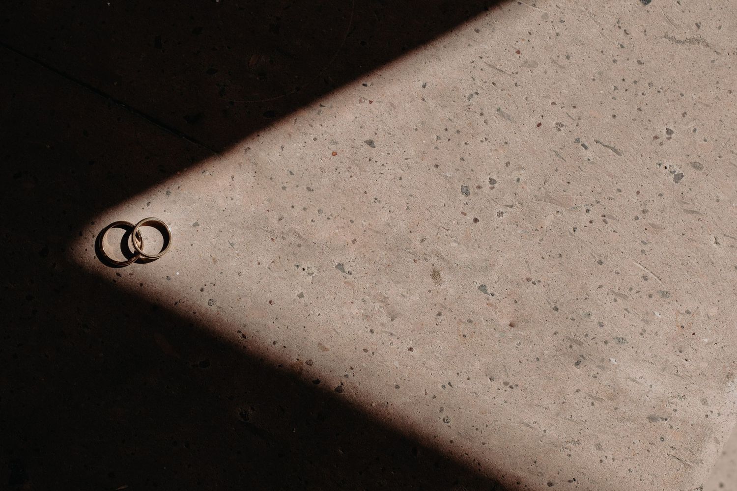 Two wedding rings casting a triangular shadow on a textured surface in black and white photography.