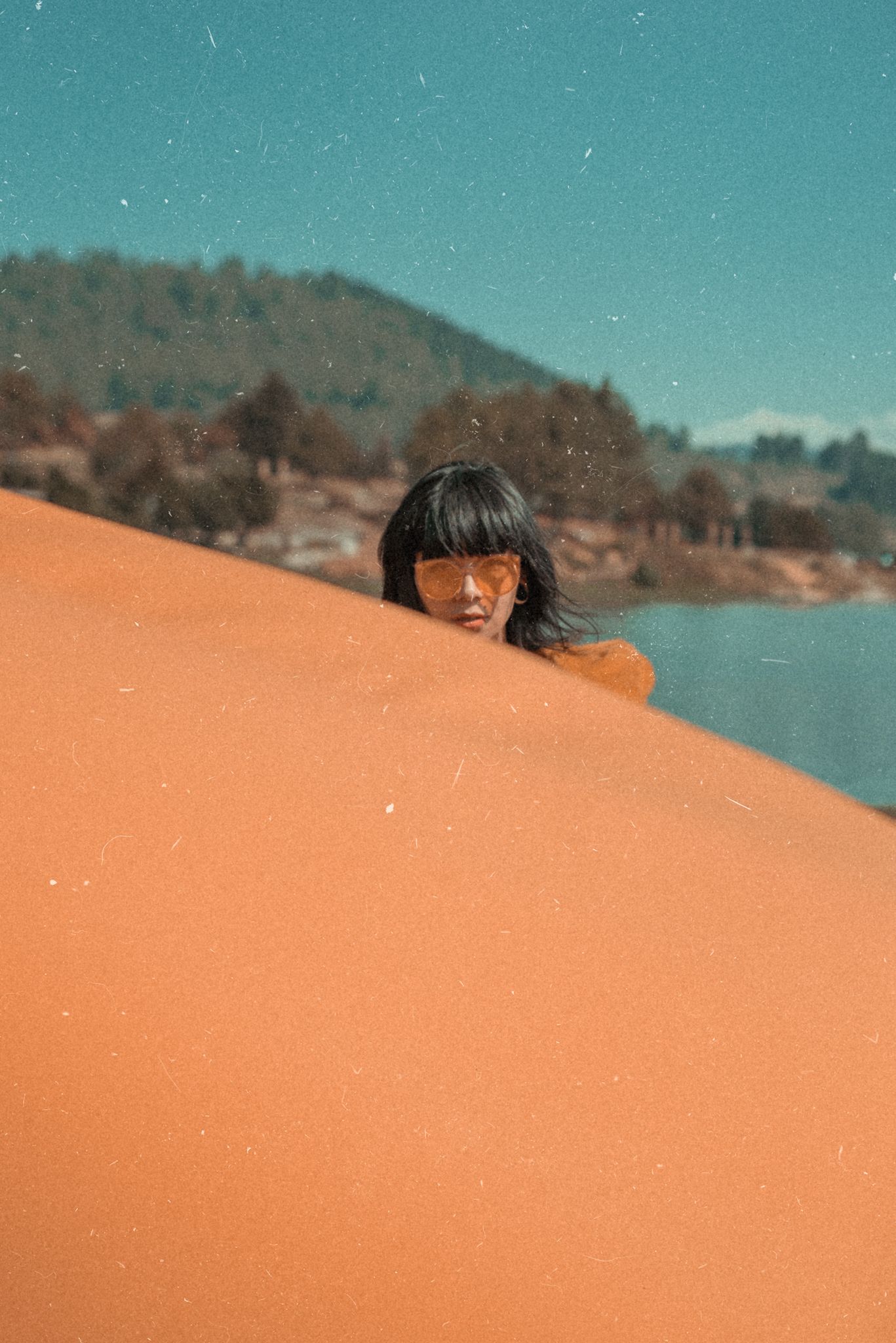 Minimalist portrait peeking over orange surface against turquoise sky.