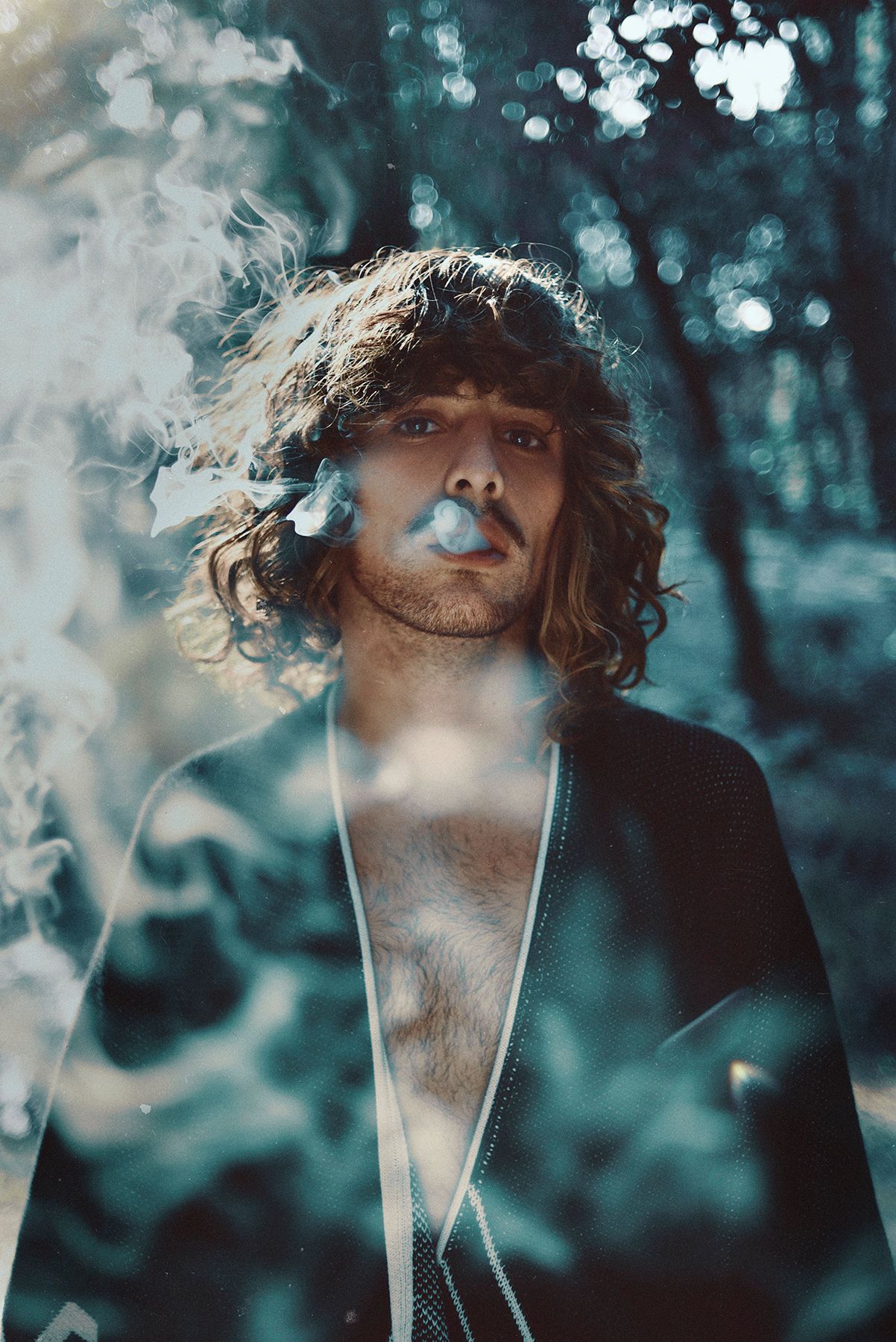 Artistic portrait with smoke effects and bokeh lighting in a moody forest setting.