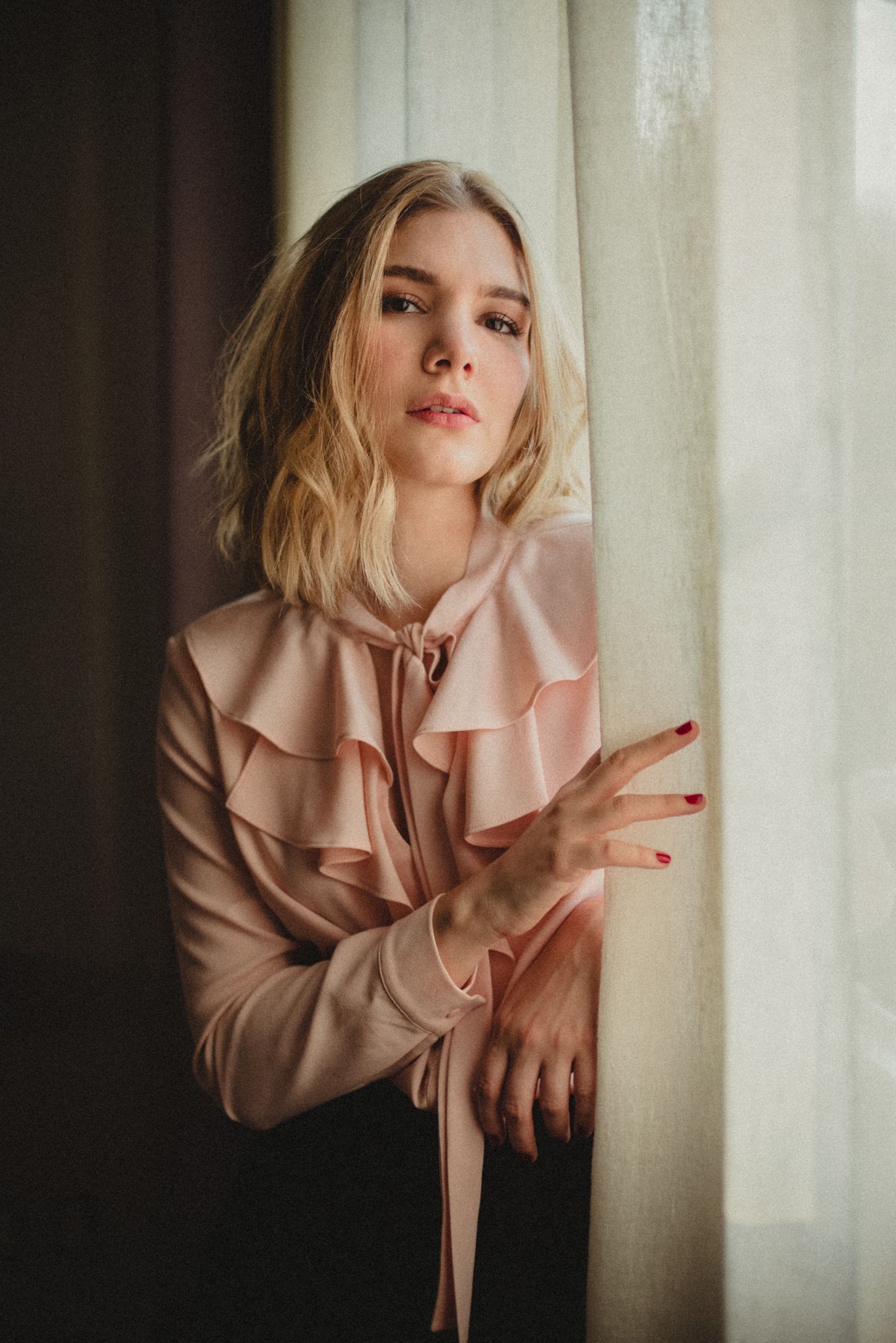Portrait of model in blush pink ruffled blouse against window light.