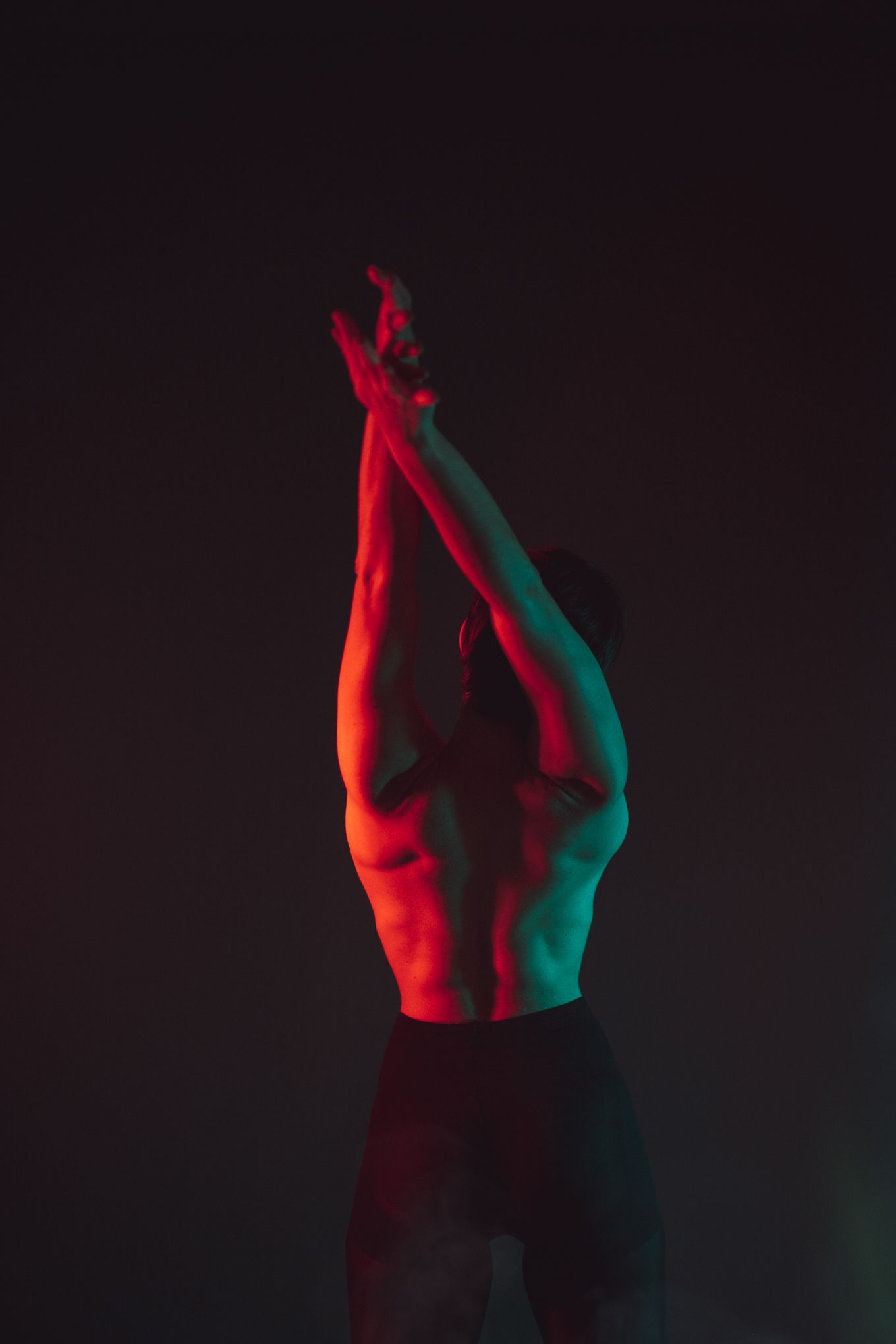 Athletic figure with raised arms bathed in contrasting red and turquoise lighting against dark background.