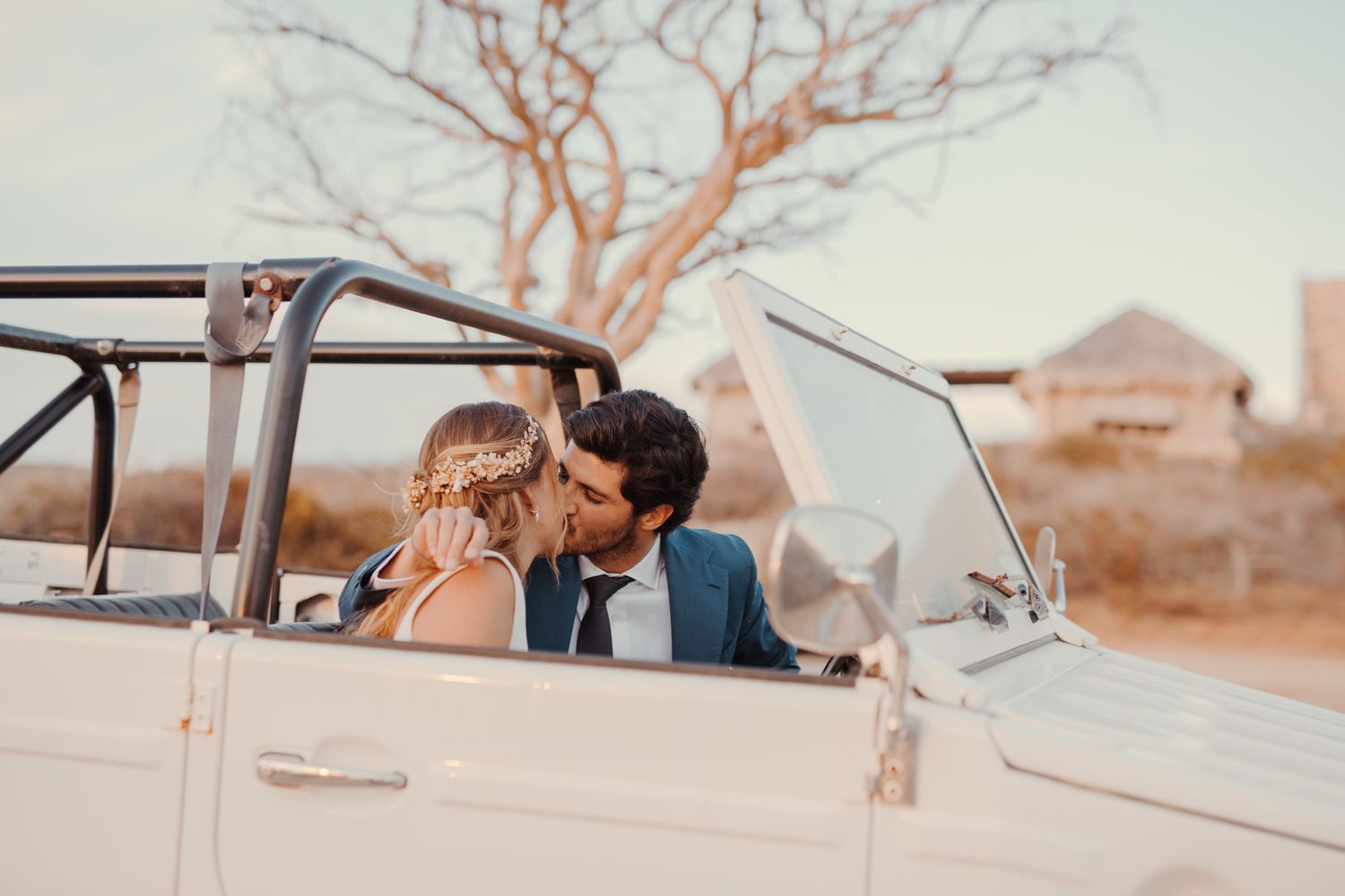Romantic couple sharing an intimate moment in a vintage convertible car at sunset in a desert landscape.