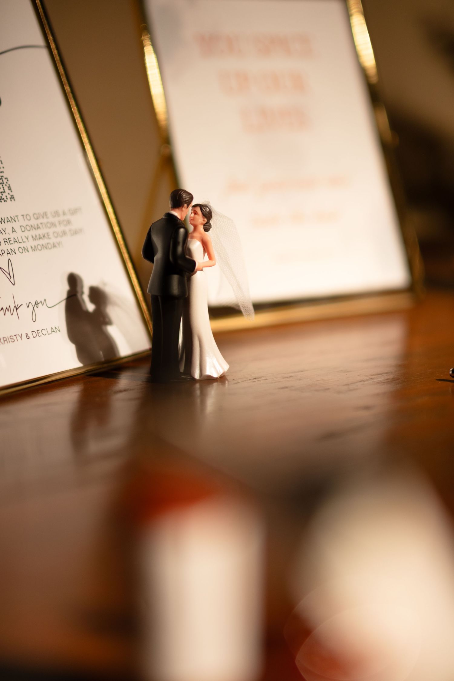 Wedding cake topper figurines casting shadows on reflective surface.