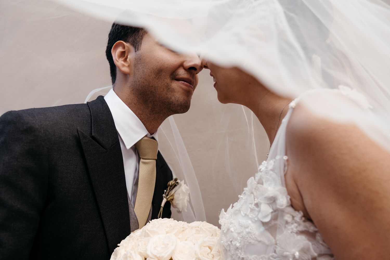 An intimate close-up shows a tender moment under a wedding veil.