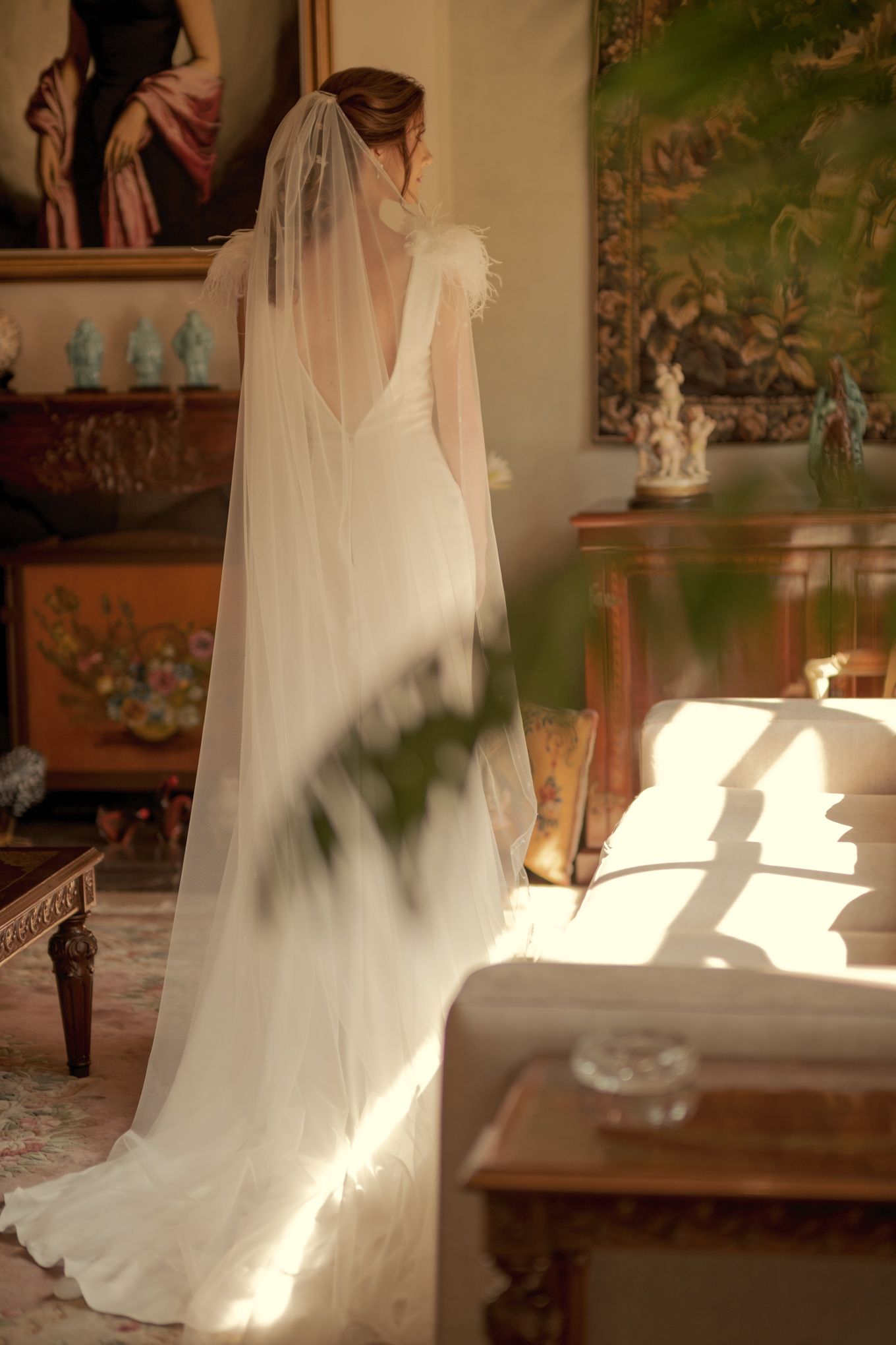 Sunlight streams through window onto bride's elegant white gown and flowing veil.