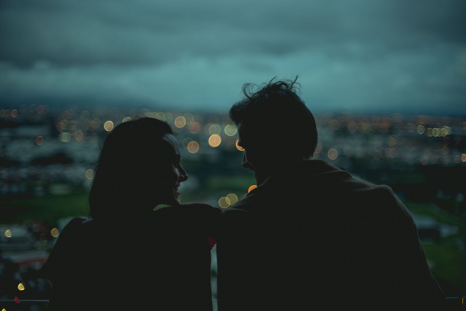 Silhouettes of two people against city lights during blue hour.