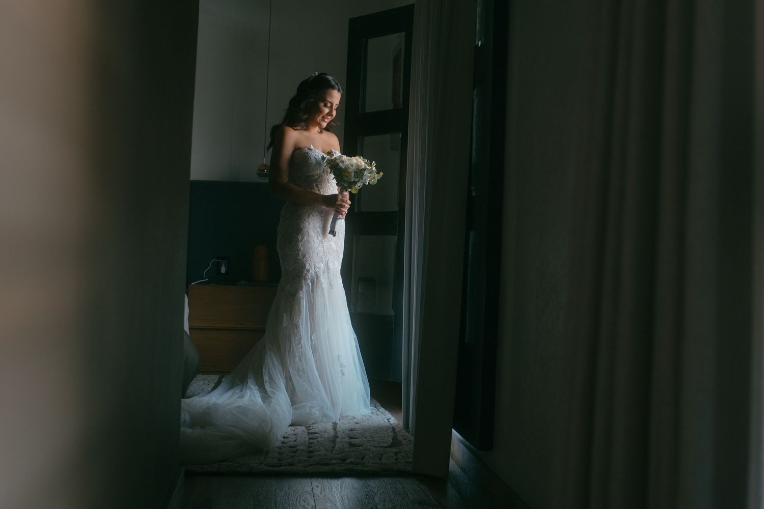 A wedding dress captured through a doorframe in moody lighting.
