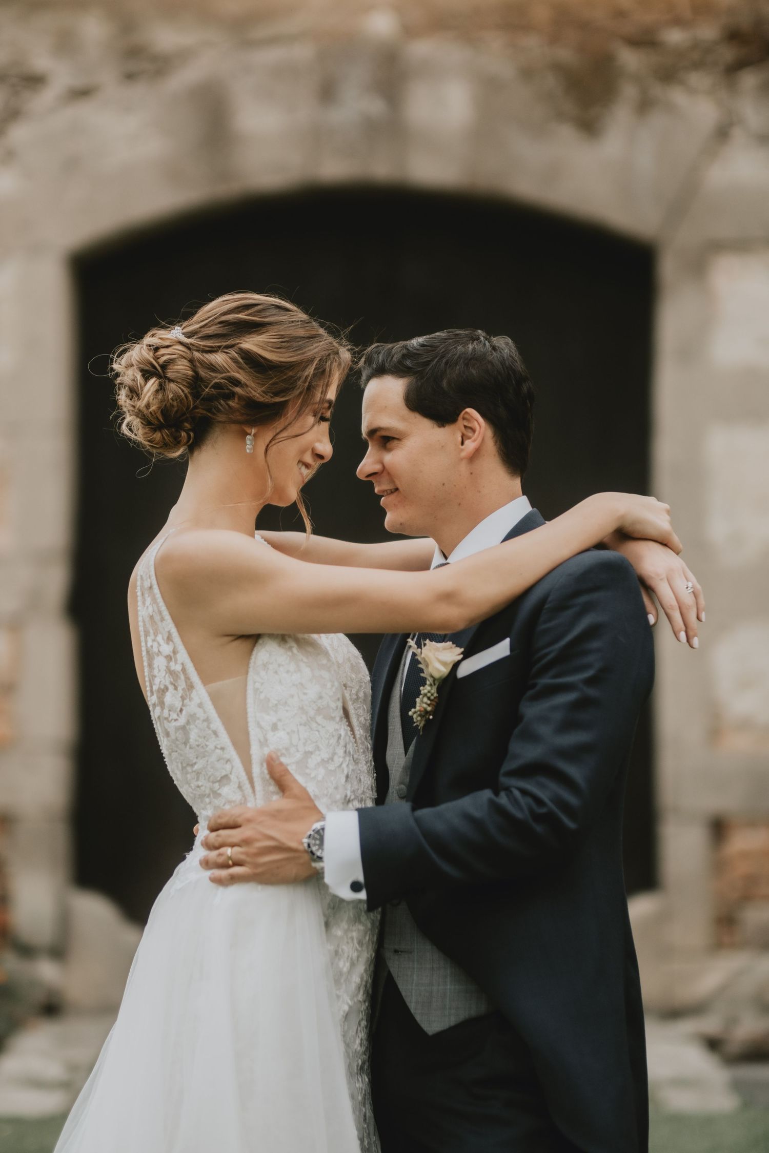 Romantic portrait of newlyweds embracing against stone archway background.