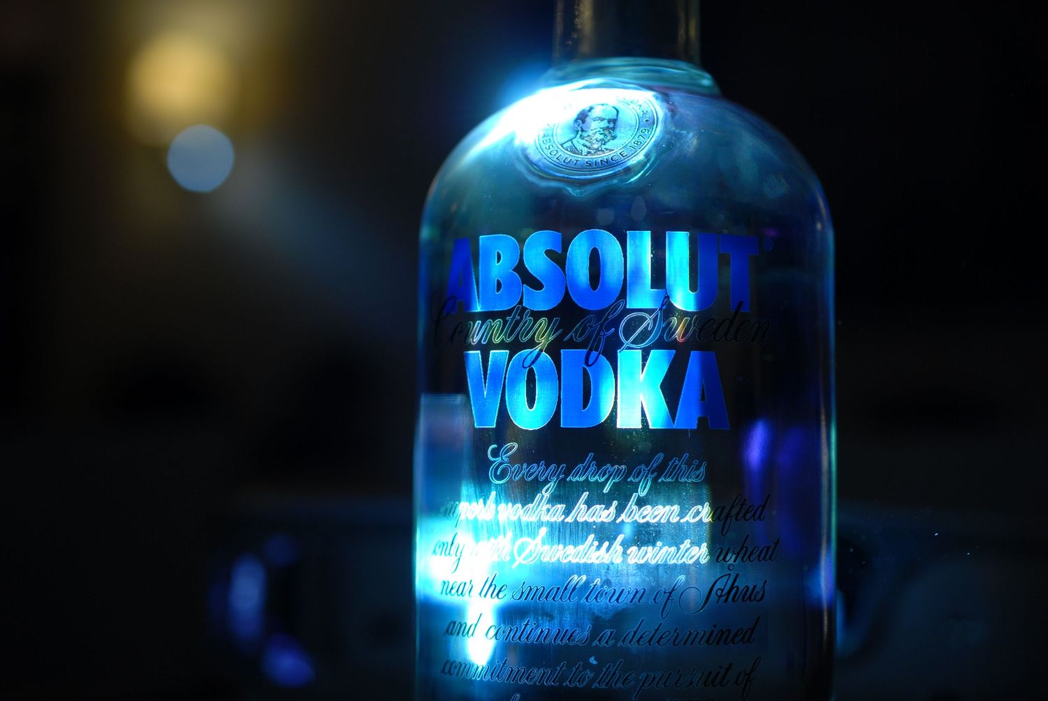 Backlit Absolut Vodka bottle glowing with blue light against dark background.