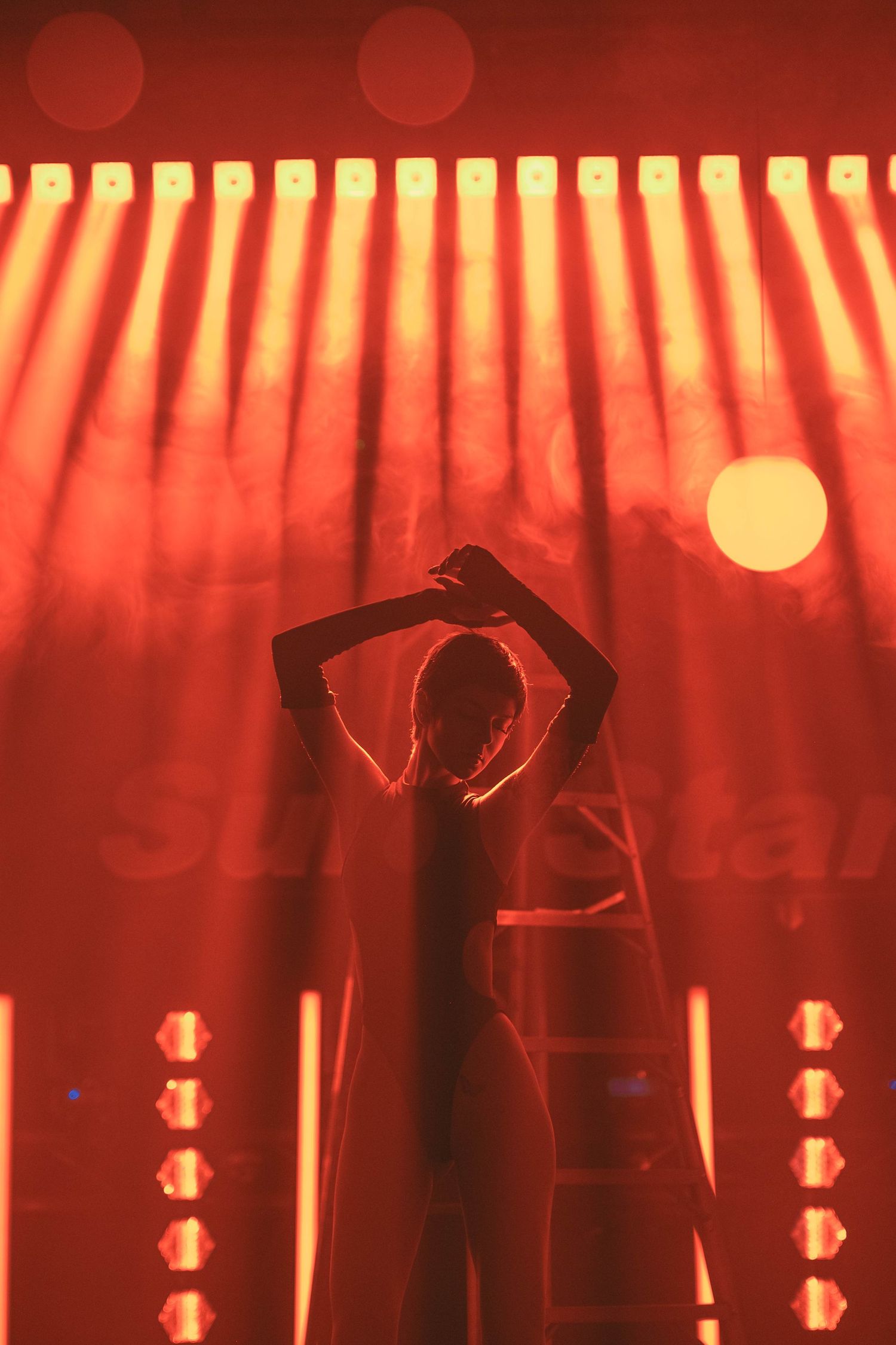 Silhouette of performer on stage with dramatic red lighting and vertical light beams.