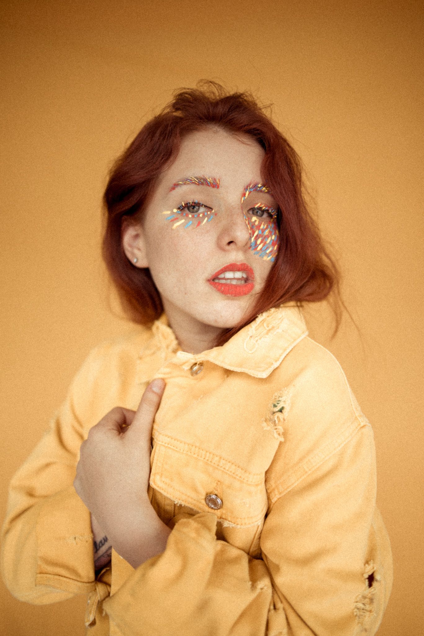 Artistic portrait in yellow jacket with face decorations against warm background.