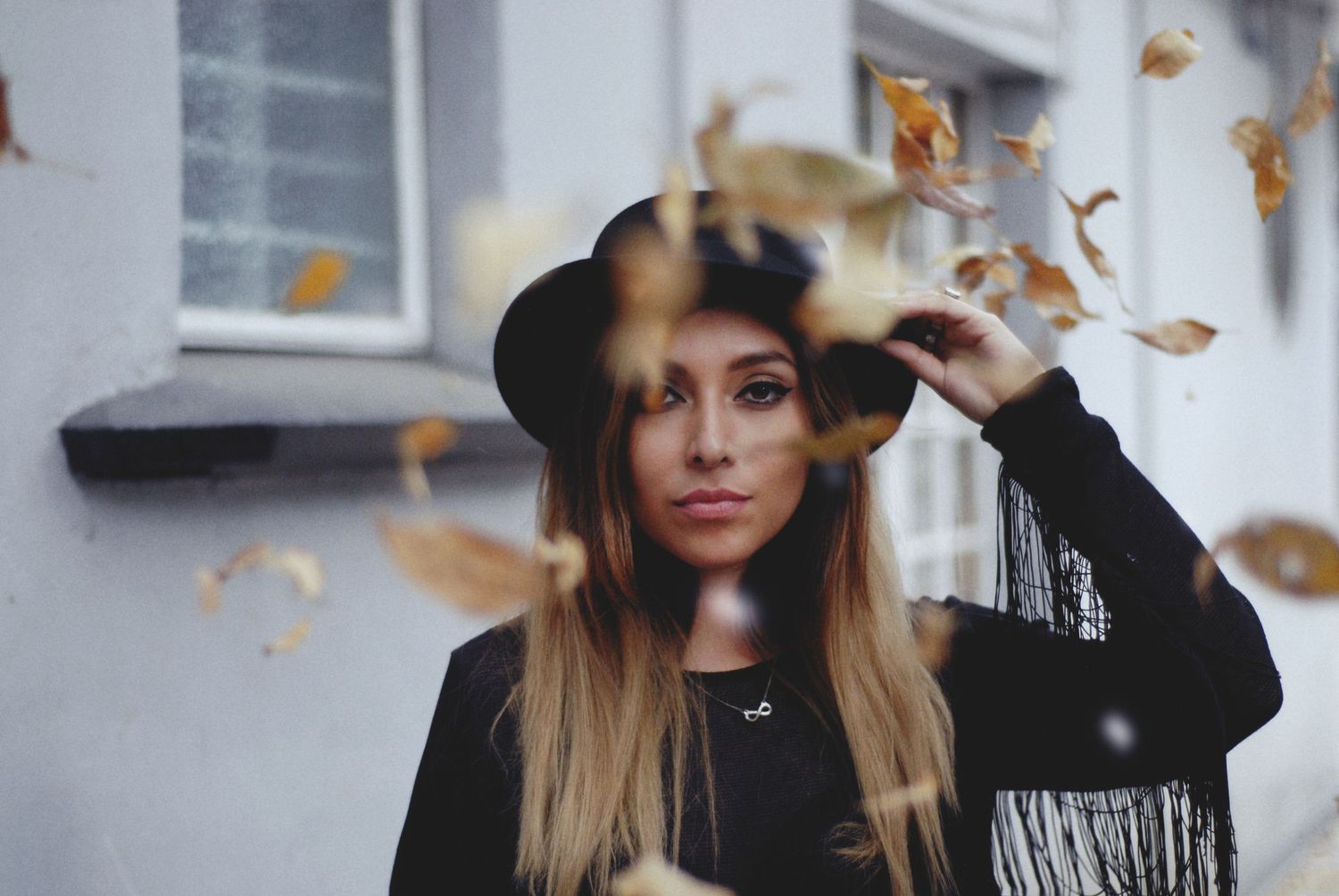 Creative portrait with falling autumn leaves against a white wall.